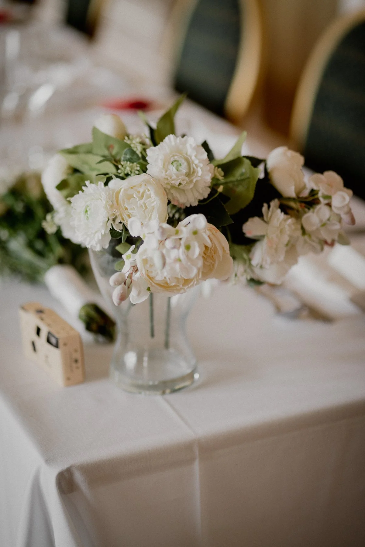 A small bouquet of white flowers in a glass vase on a white table with a white tablecloth.