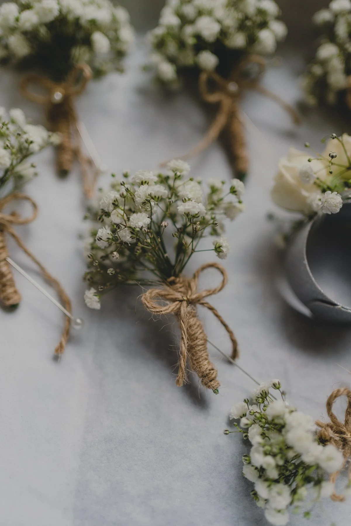 Close-up of small white flower bouquets wrapped with twine, with metal pins and a cup in the background.