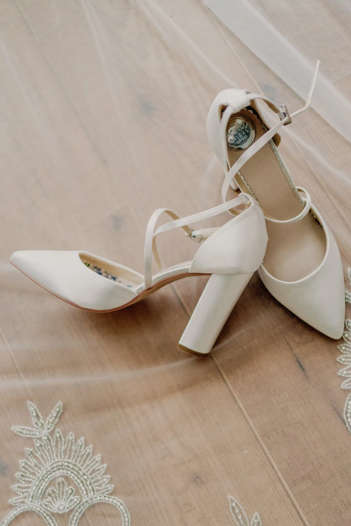 White high-heeled shoes with ankle straps on a wooden floor.