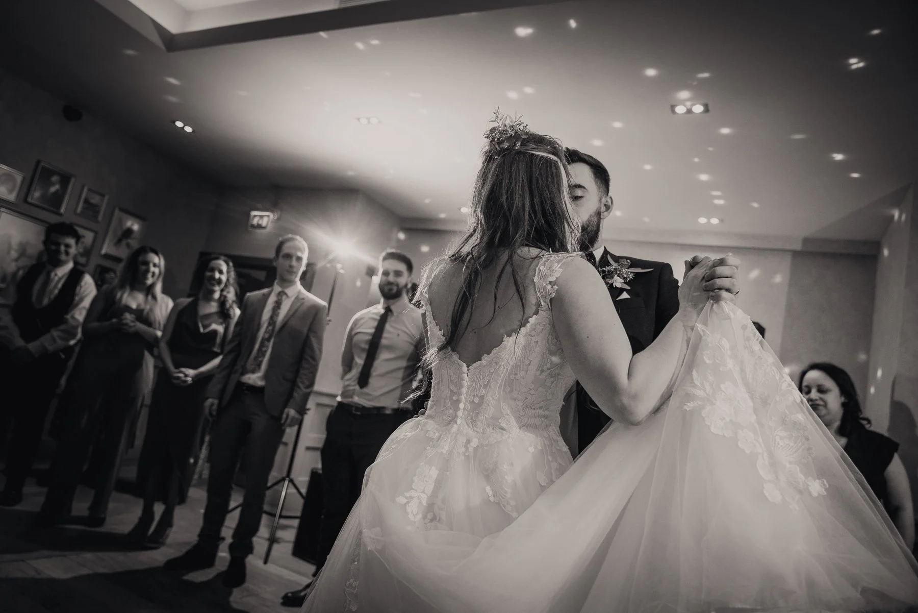 A bride and groom sharing their first dance at a wedding reception, with guests watching in the background.