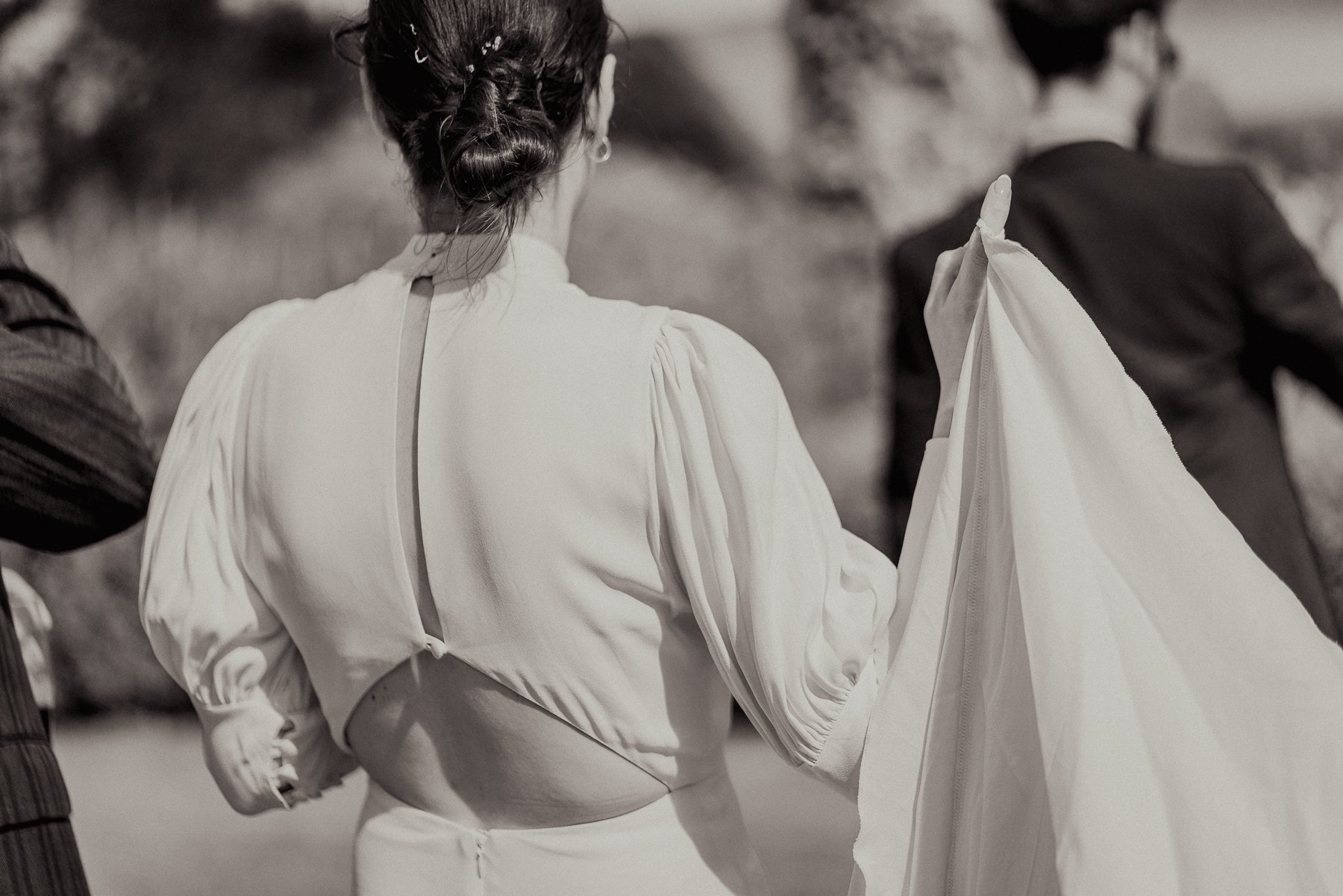 Back view of a woman with braided hair wearing a long-sleeved, light-colored top and holding a light-colored fabric or garment.