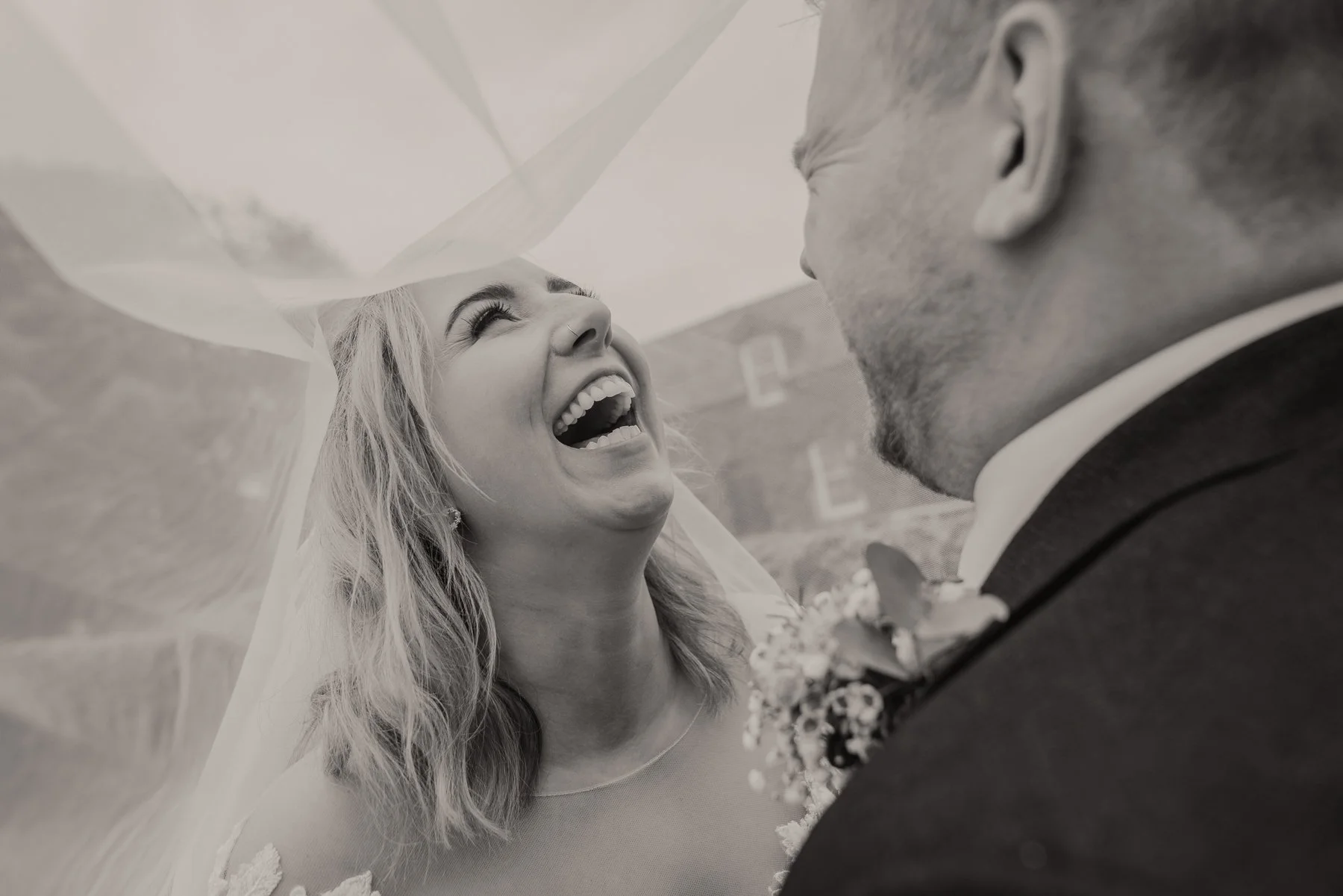 A woman in a wedding dress is smiling and laughing with a man dressed in a suit, sharing joyful moment during a wedding ceremony.