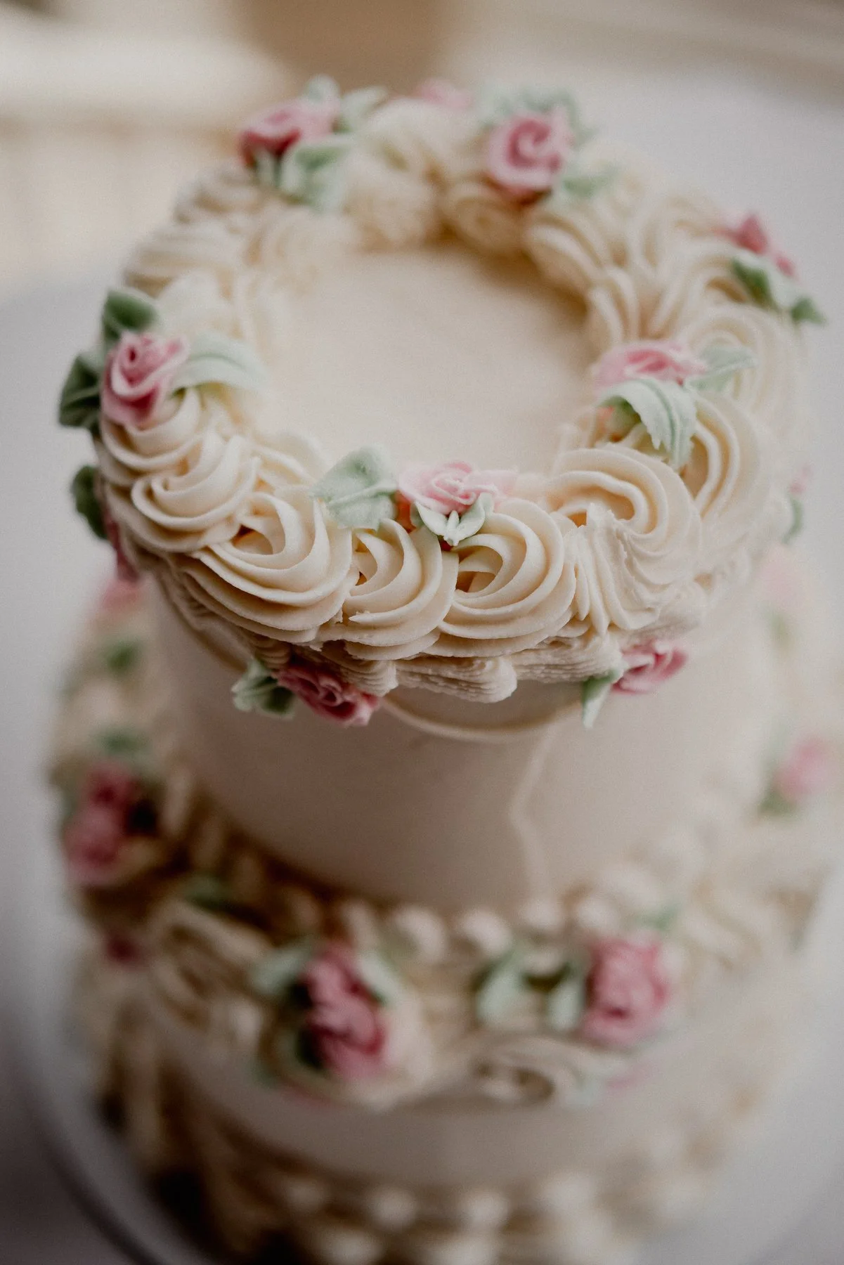 Close-up of a white frosted cake decorated with pink and green floral icing.