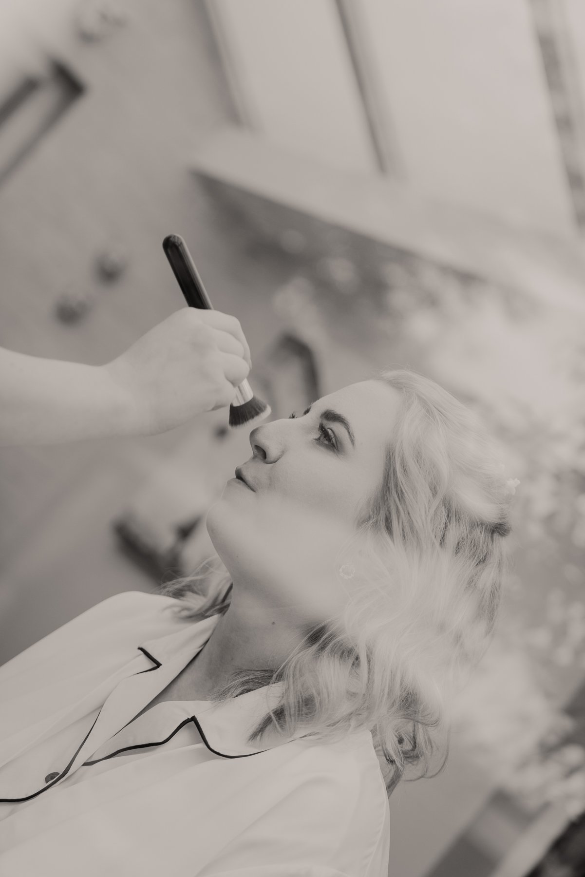 A woman with light-colored, wavy hair relaxing in a beauty clinic as a professional applies makeup or cosmetic product near her nose.