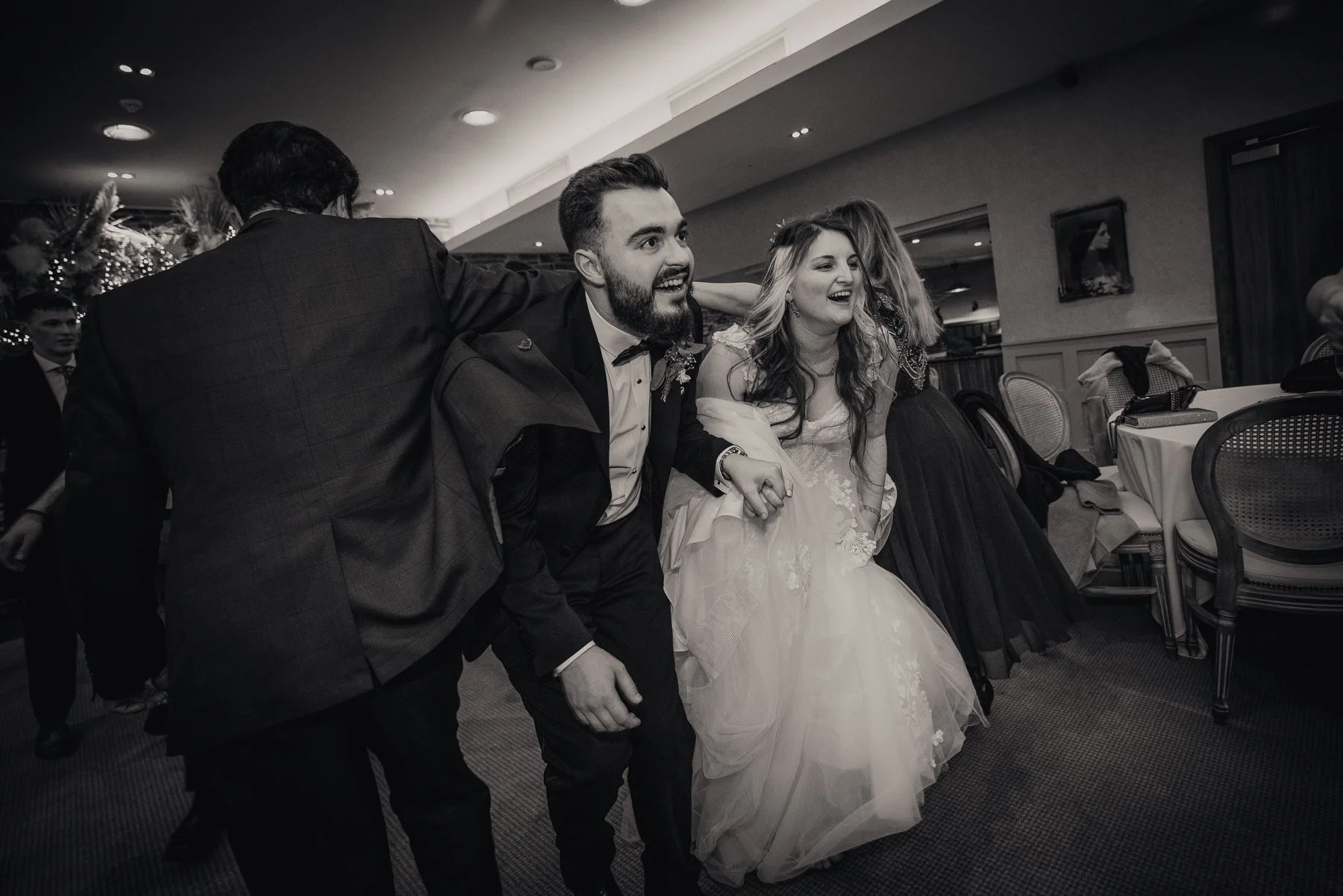 People dancing and celebrating at a wedding reception, including a groom and bride holding hands, smiling and enjoying the moment.