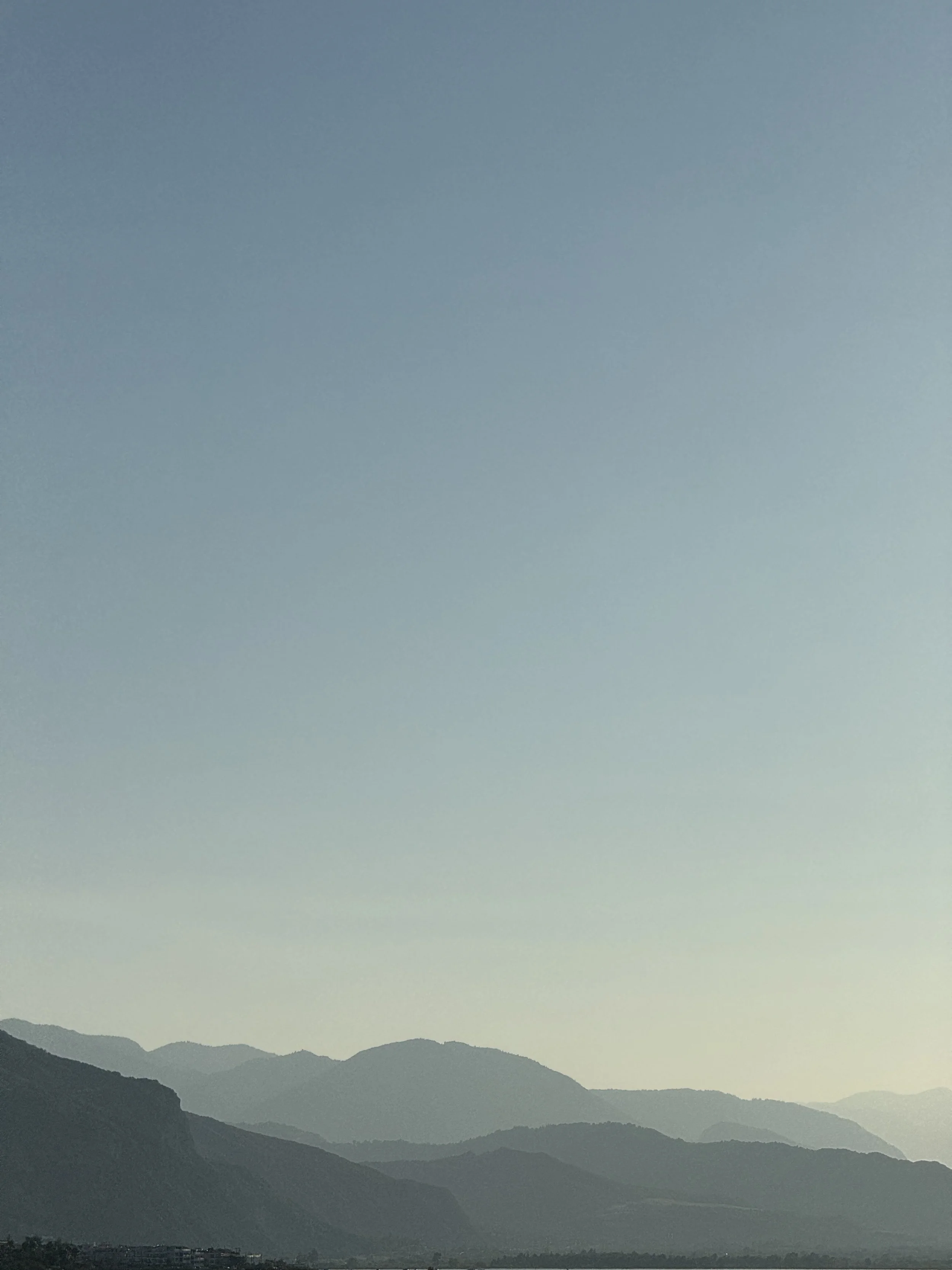 Scenic view of distant mountain range under a clear sky with a gentle gradient from blue to green, with a small town at the base of the mountains.