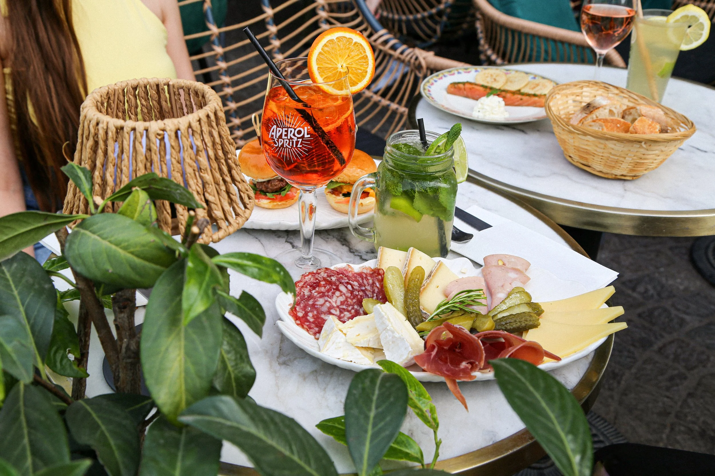 Un plateau de nourriture avec des fromages, charcuteries, et légumes, accompagné de cocktails avec des tranches de citron et de concombre, sur une table de fête en plein air.