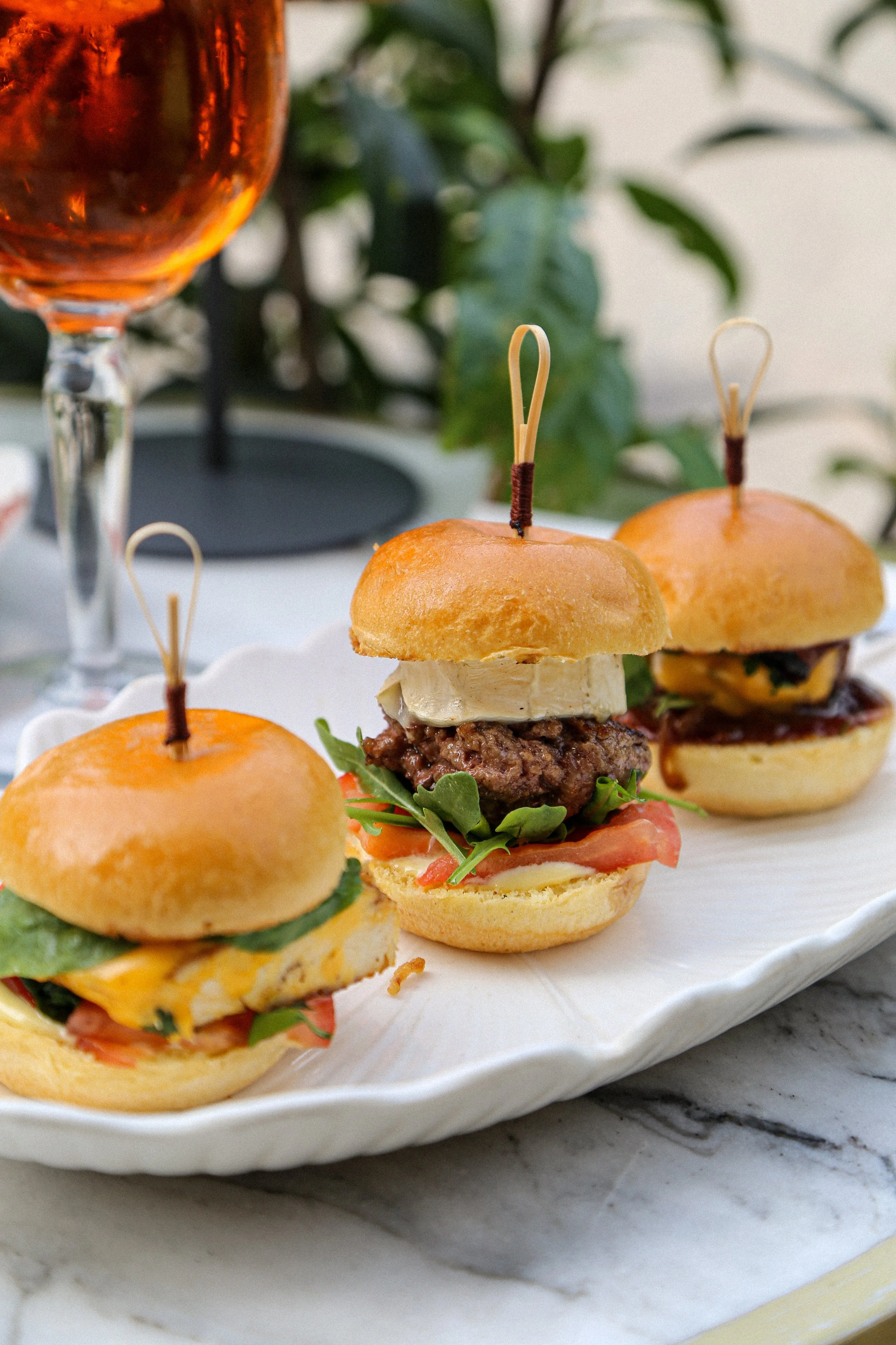 Mini-burgers avec légumes, fromage et viande, servis sur une assiette blanche.