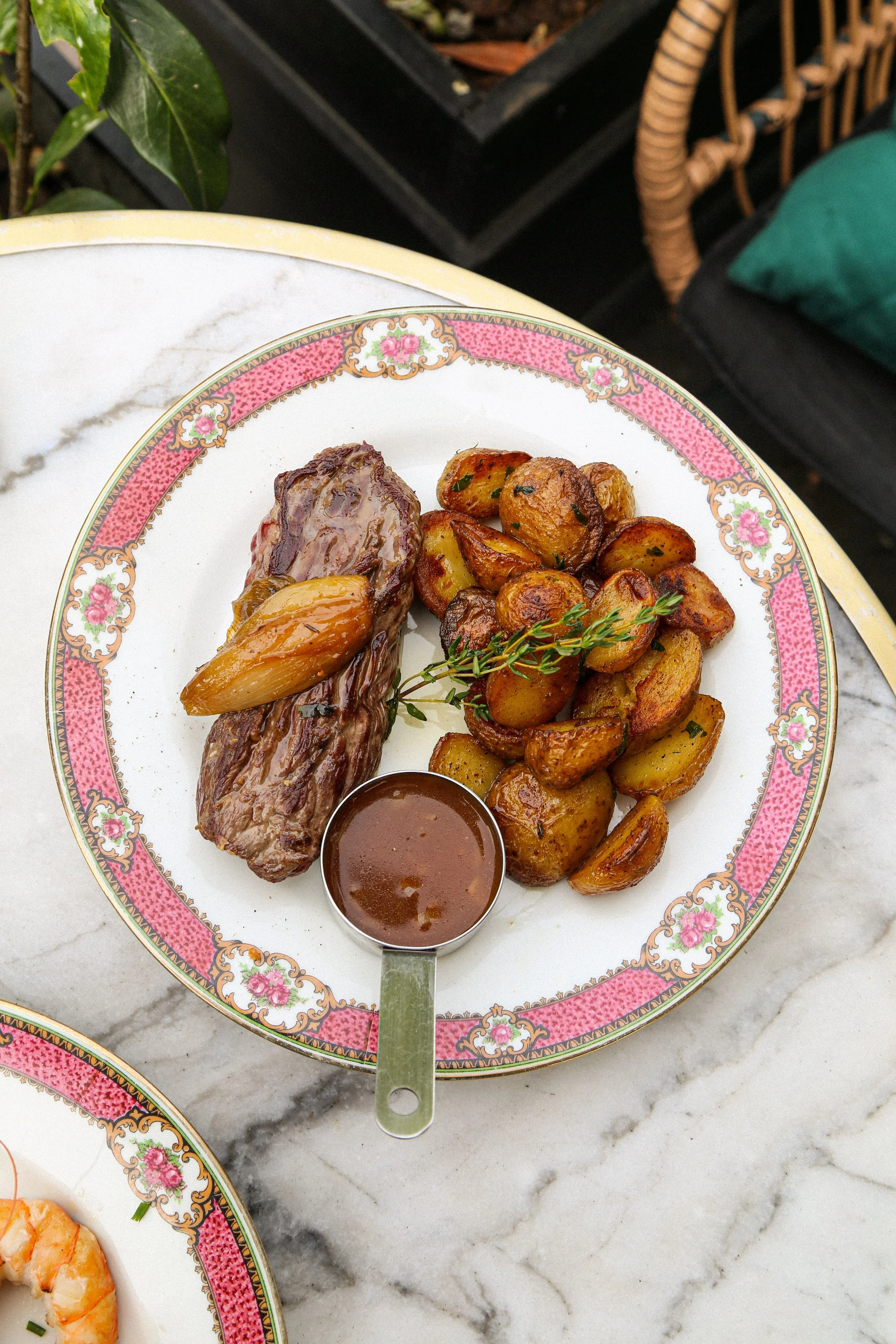 Plate avec côtelettes de bœuf, pommes de terre rôties, branche de thym, sauce en bol, sur une table en marbre.