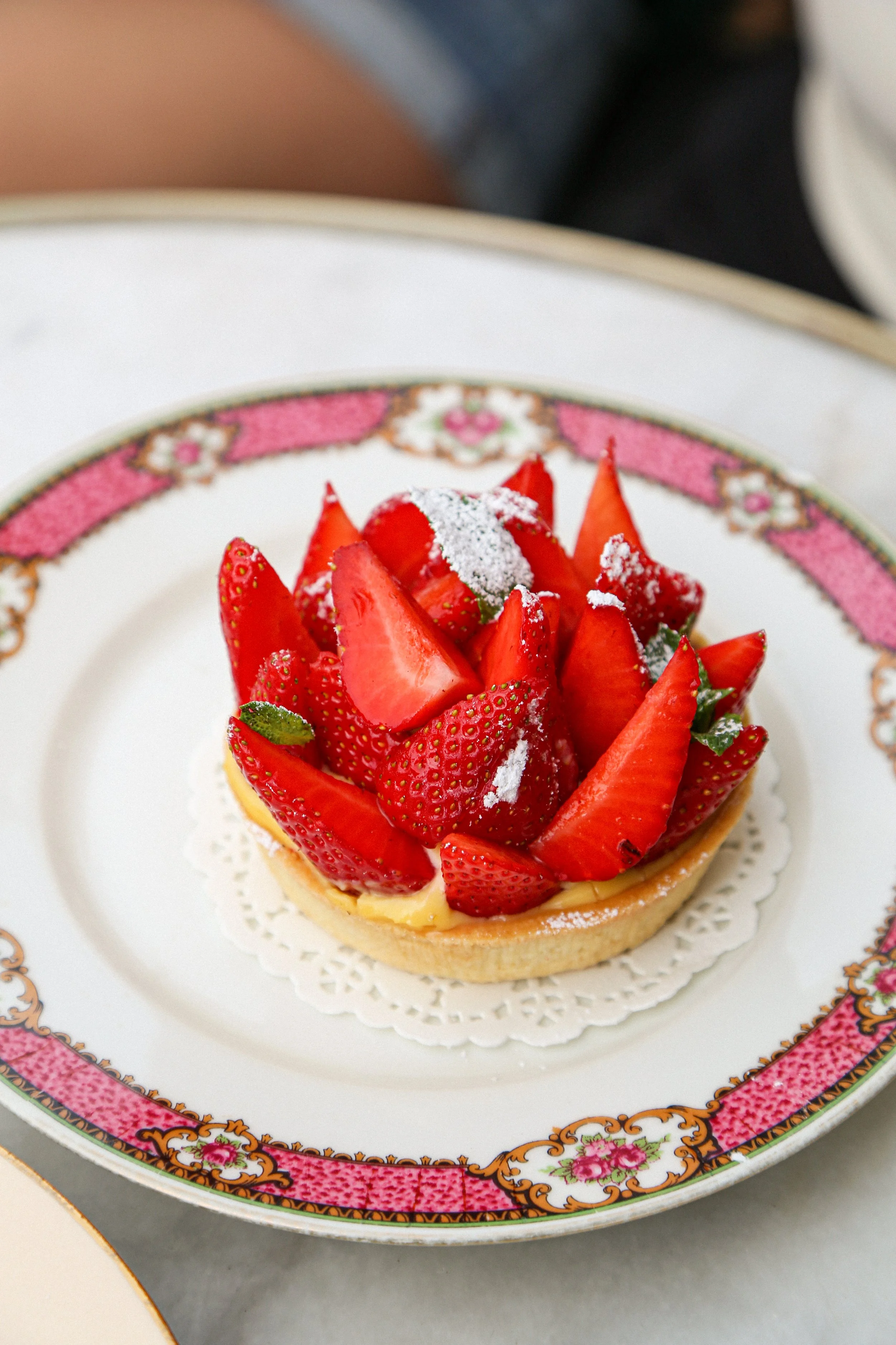 Gâteau aux fraises décoré avec des fraises coupées en tranches, saupoudré de sucre glace, placé sur une assiette ornementée.