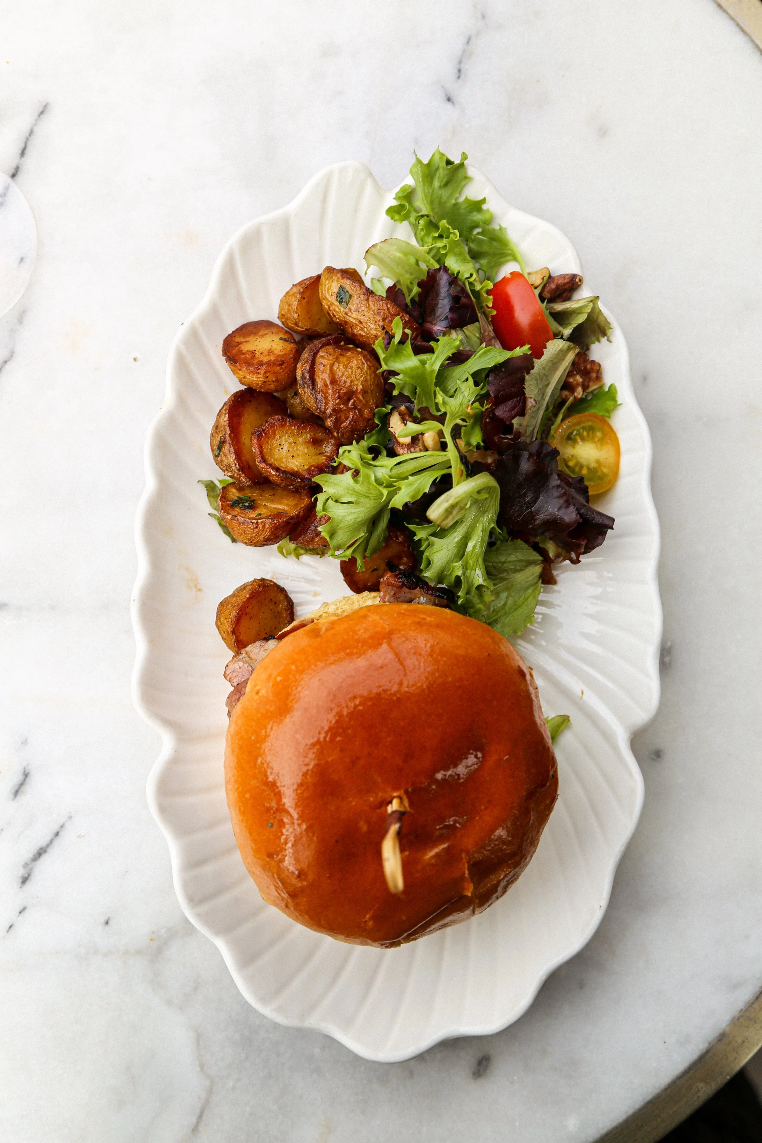 Salade verte avec tomates cerises, pommes de terre rôties, et un burger avec un petit pain doré.