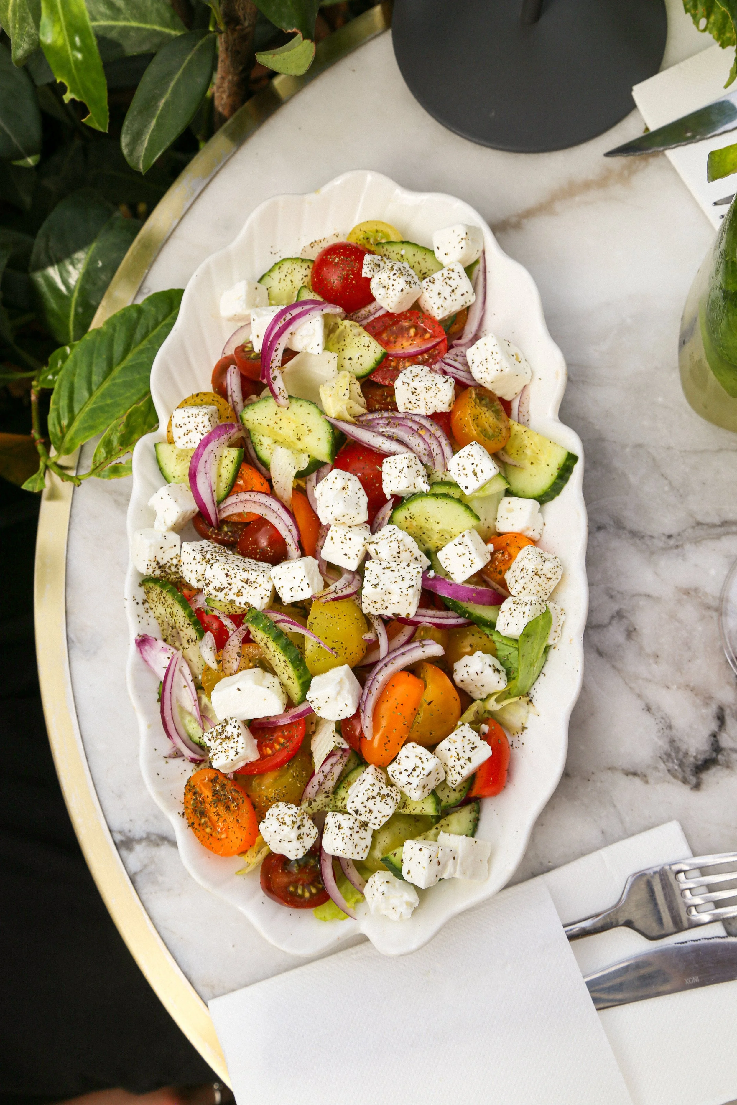 Salade de légumes frais avec tomates, concombres, oignons rouges, poivrons, cubes de feta, poivre noir, servie dans une assiette blanche sur une table en marbre.