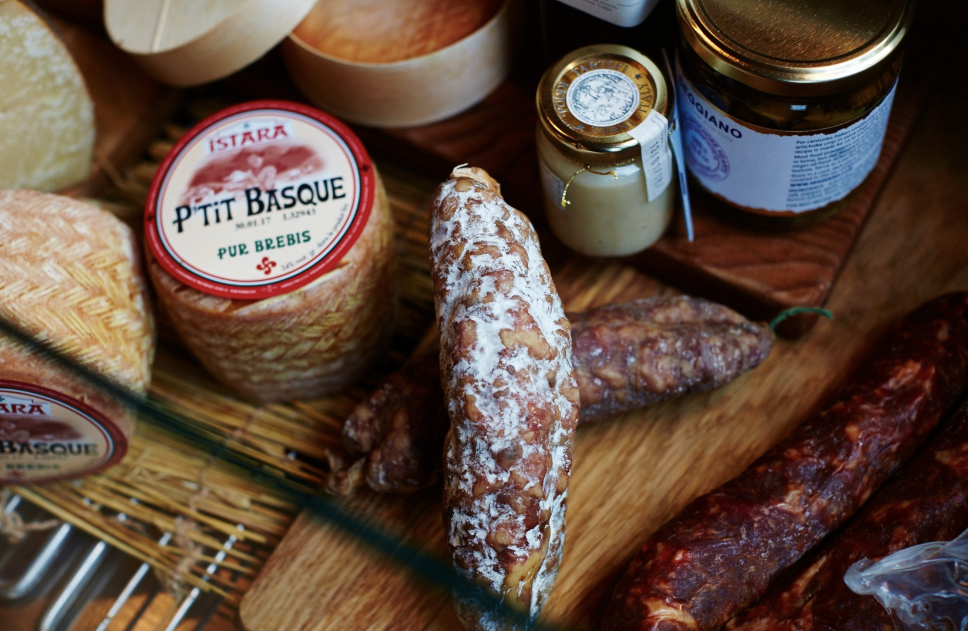 Delicious artisan French cheeses, cured meats, saucisson and luxury deli products on a wooden tray.