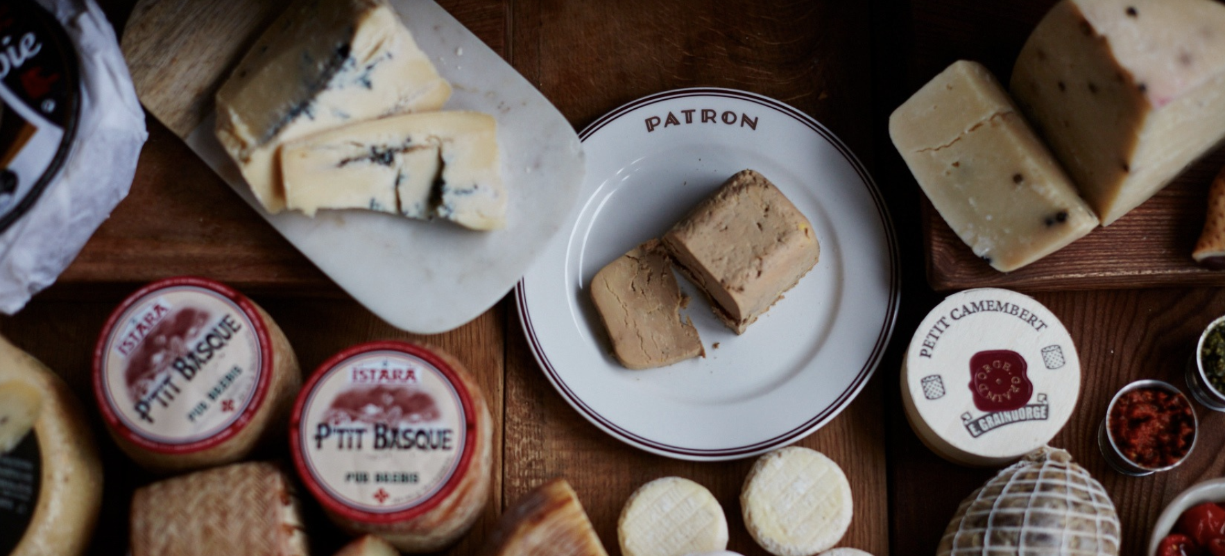 An assortment of delicious French cheeses, including blue cheese, soft and hard cheeses, alongside velvety pâtés and other luxury deli items on a wooden table.