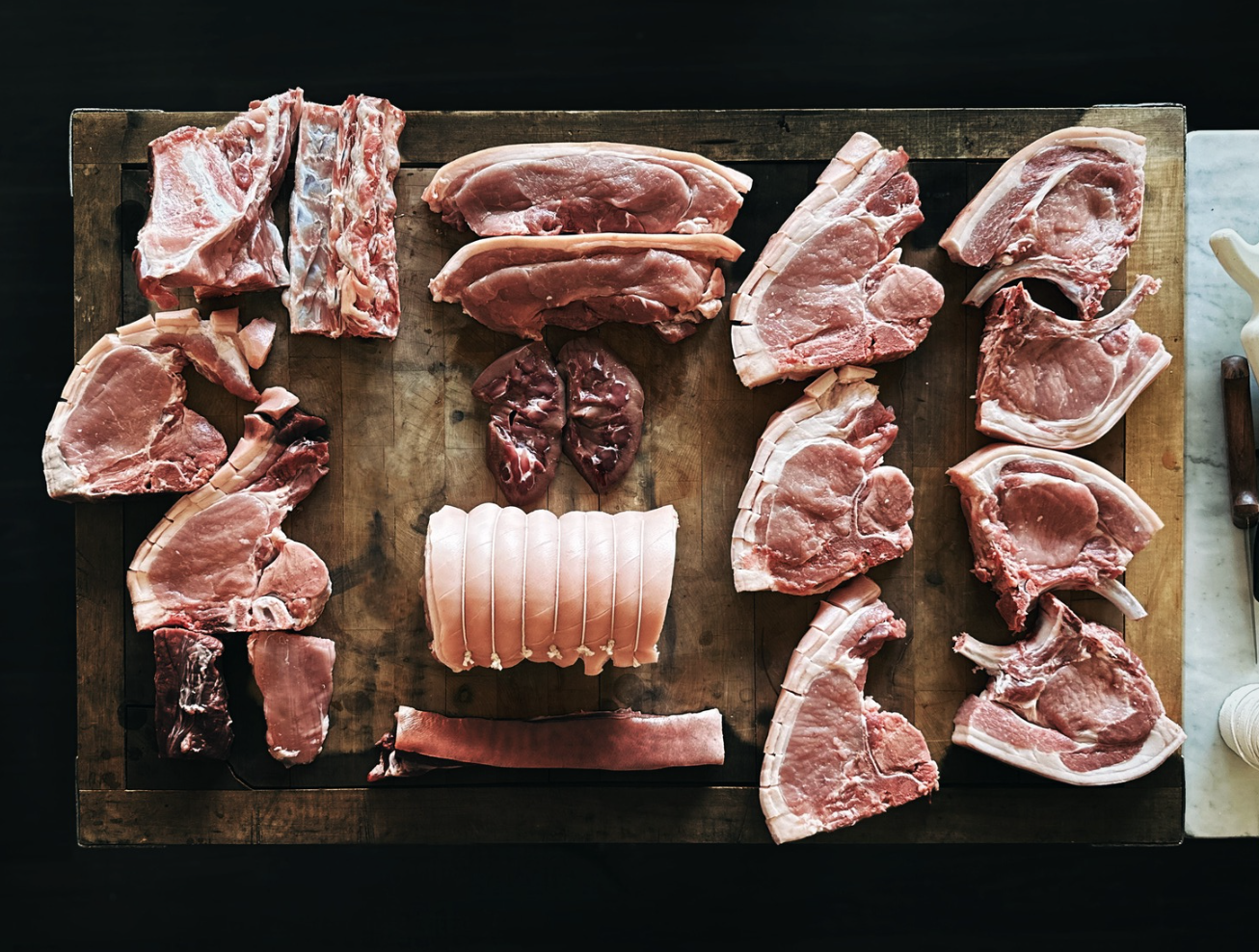 Various cuts of raw pork arranged on a wooden cutting board, at one of Patron's chef butchery classes.