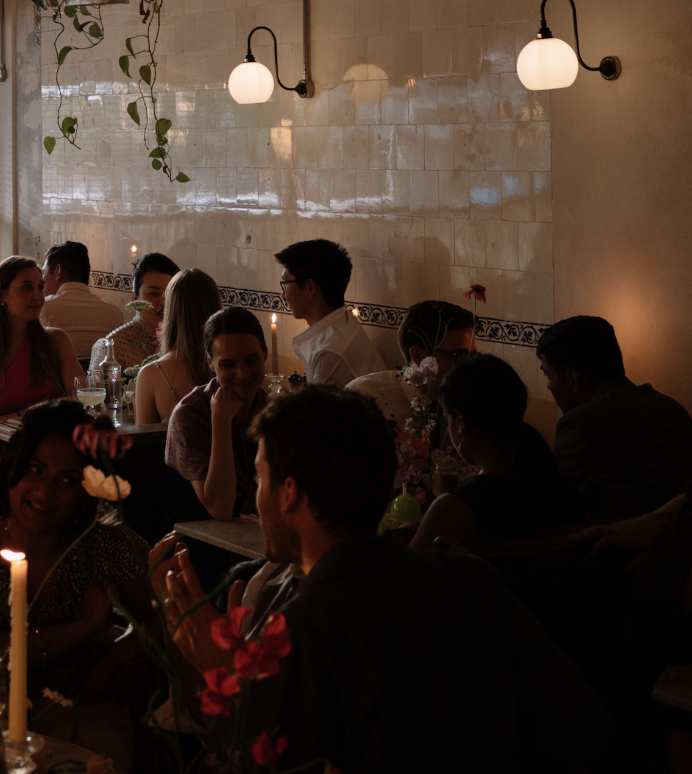 A lively private party at Patron's dining room, with people gathered around marble tables in a dimly lit restaurant, decorated with flowers and illuminated by ambient light and candles.