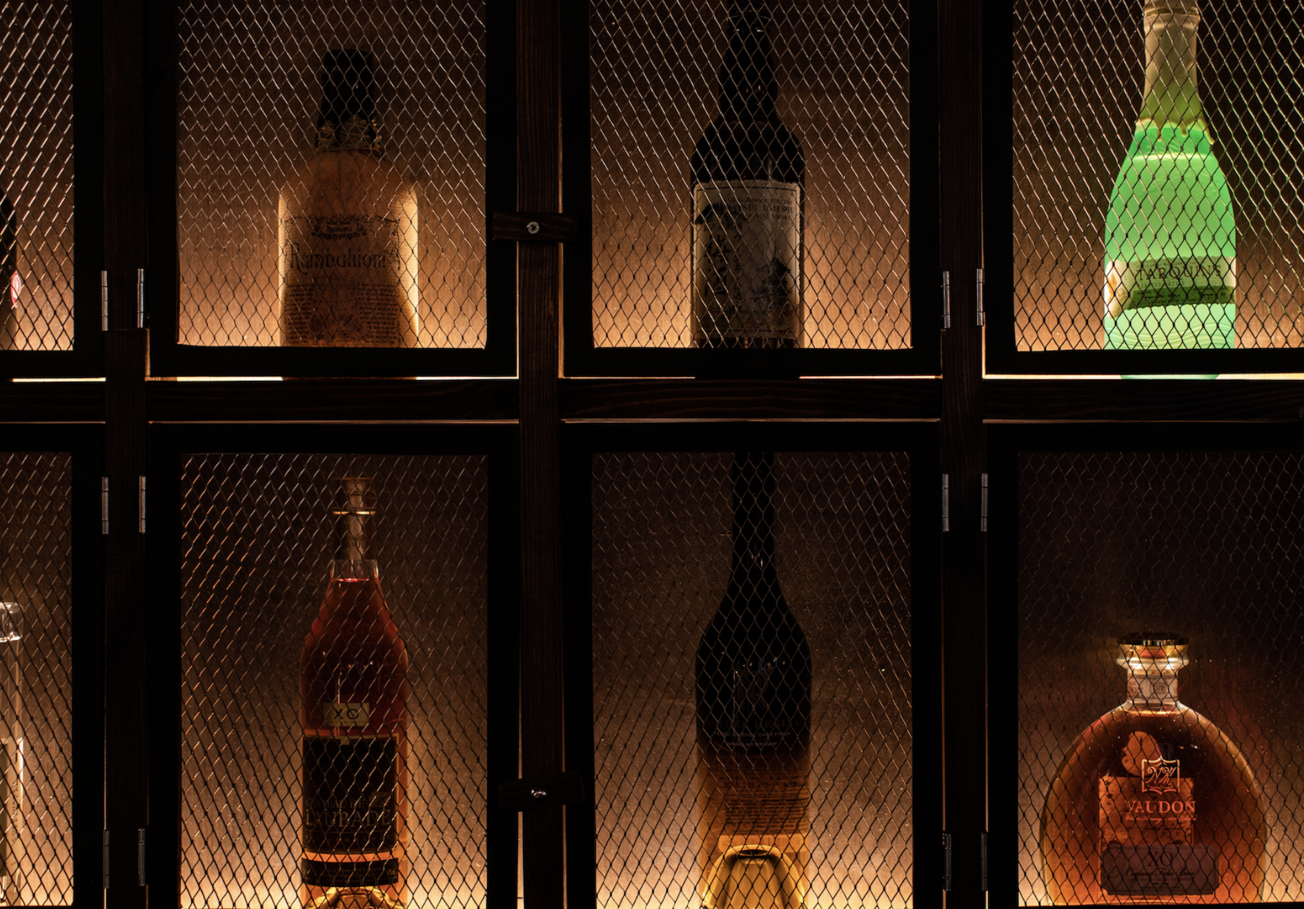 A stunning black metal cabinet in the 1920s lounge, containing bottles of high-end spirits, illuminated by warm glowing light.