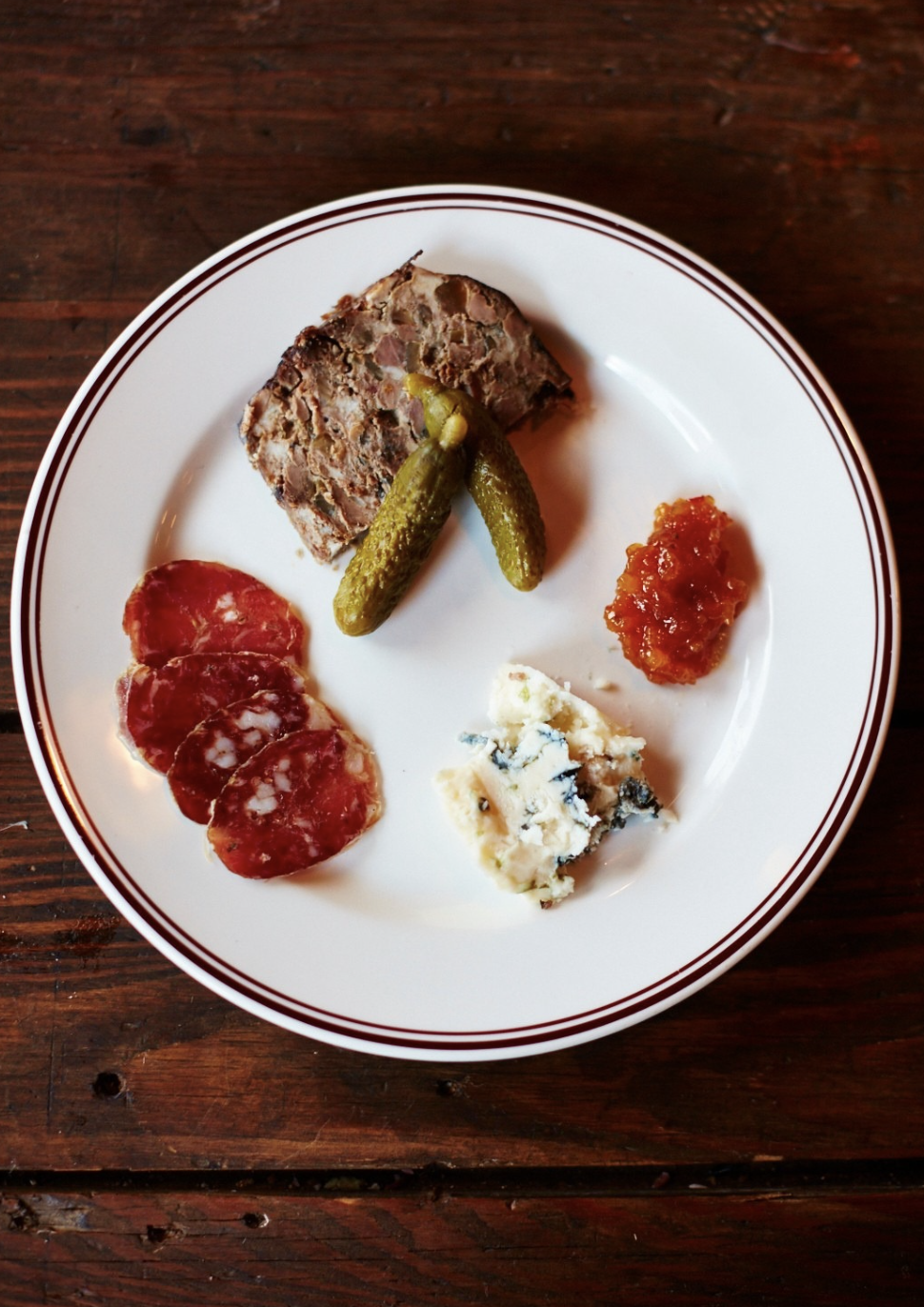 A plate of delicious French saucisson, cured meats, pickles, cornichons, a serving of velvety pâté, a dollop of chill jam, and a piece of blue cheese.
