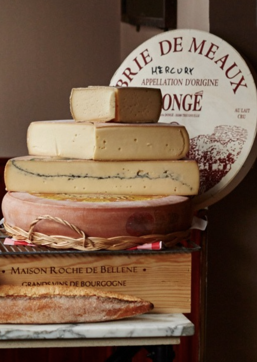 Large blocks of incredible artisan French cheeses laid out one on top of the other on a marble table.