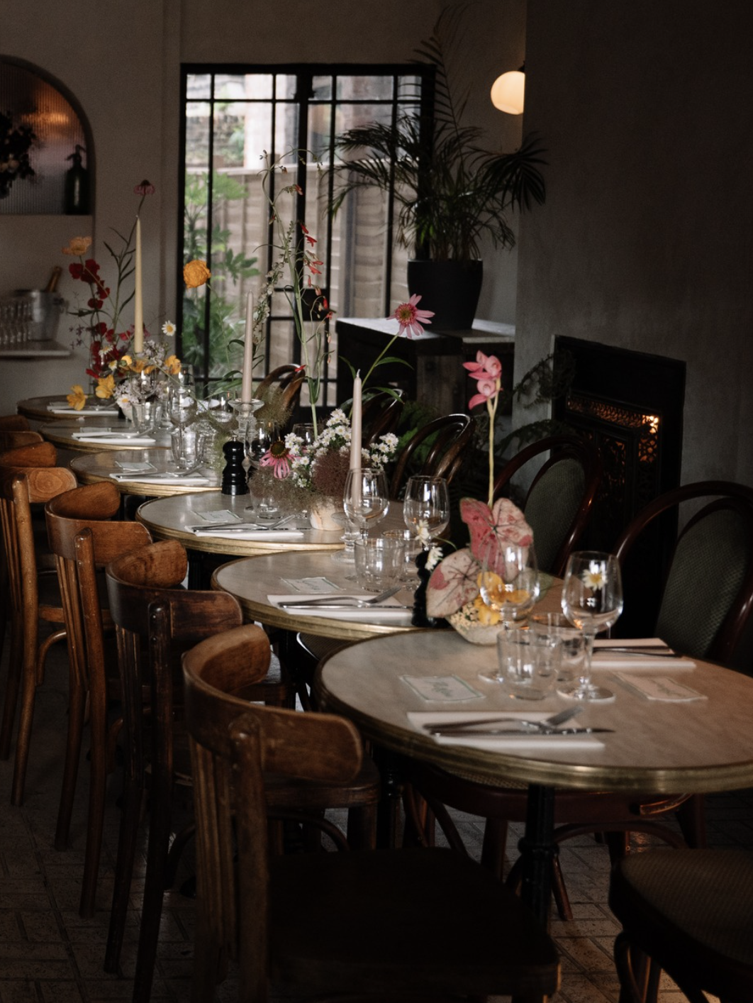 Elegant dining table set for a wedding party, with floral arrangements, candles, and glassware, in a softly lit private dining room with a hidden door and exclusive access to a secret garden.