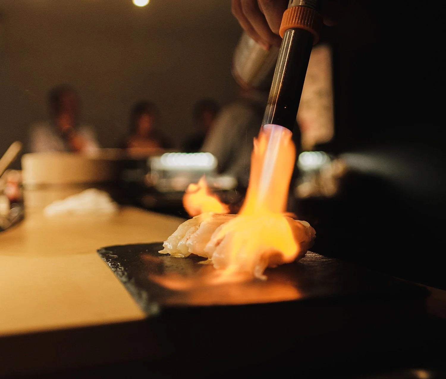 The Table. Private dining. Fine Dining. Culinary journey. Chef flaming a dish with a kitchen torch.