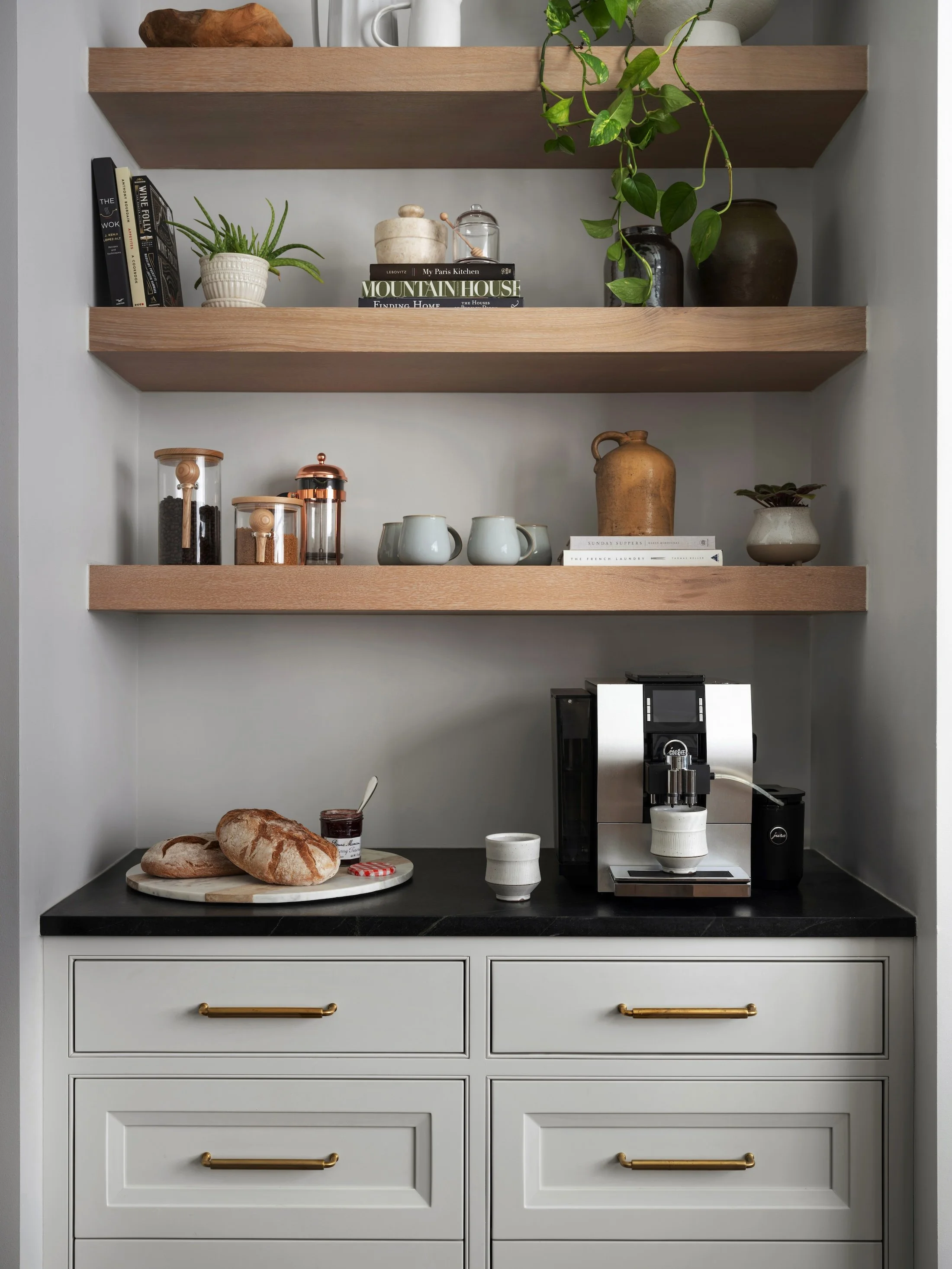 Built-in coffee bar with floating wood shelves, white cabinetry, black countertop, and brass hardware.