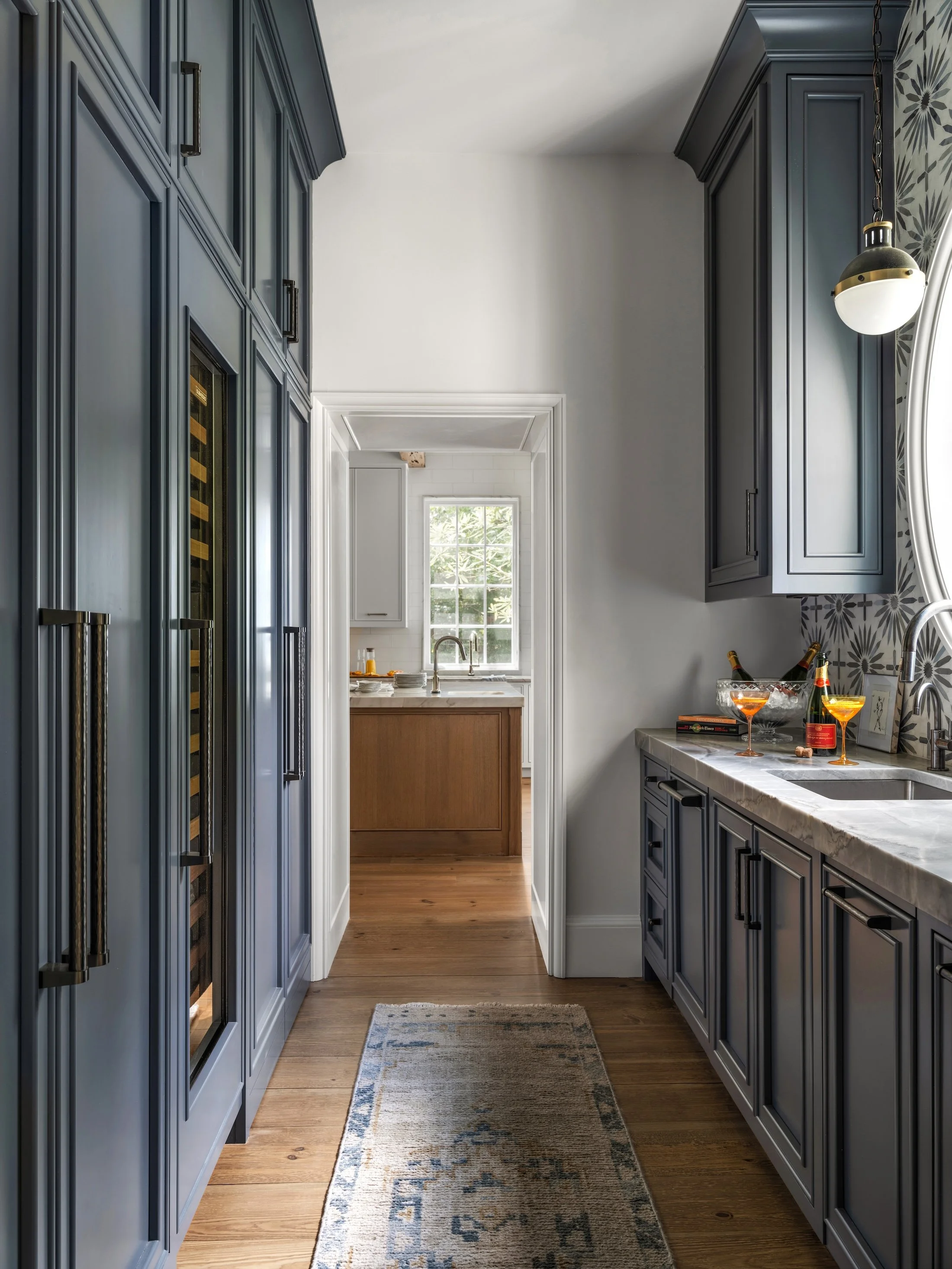 Moody blue butler’s pantry with floor-to-ceiling cabinetry, dark countertops, and a view into the adjoining kitchen.
