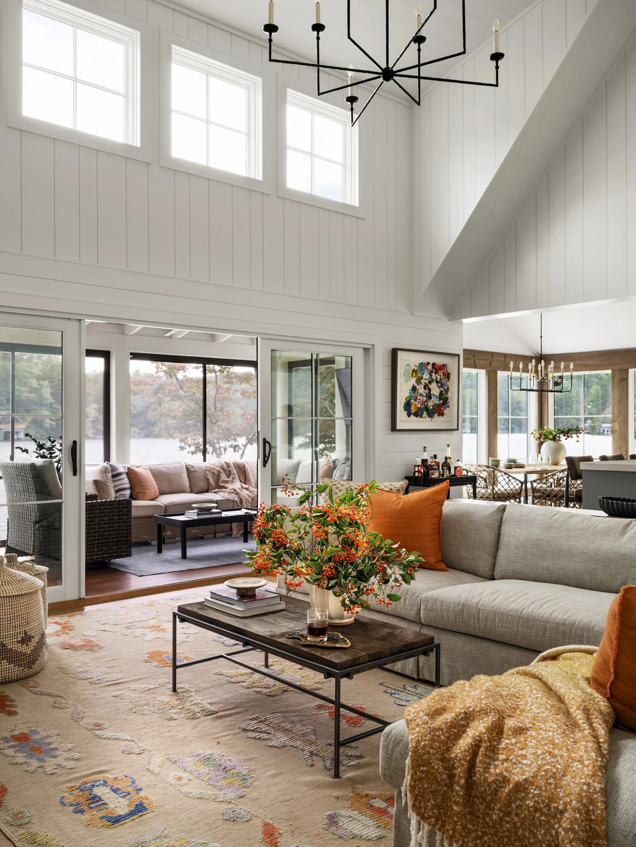 Vaulted living room with layered neutral furnishings, patterned textiles, large windows, and views into the adjoining porch.