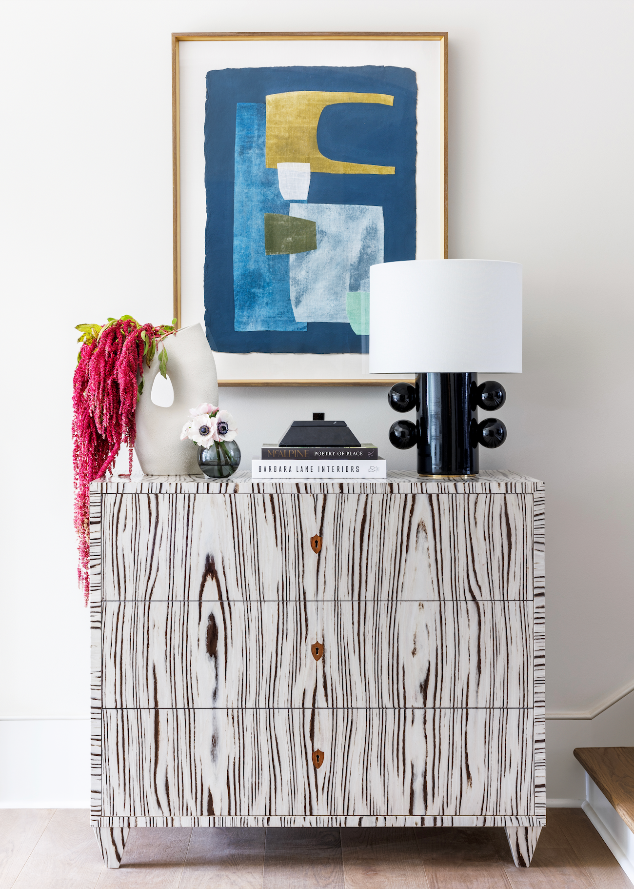Patterned console cabinet styled with abstract artwork, books, a table lamp, and colorful decorative accessories.