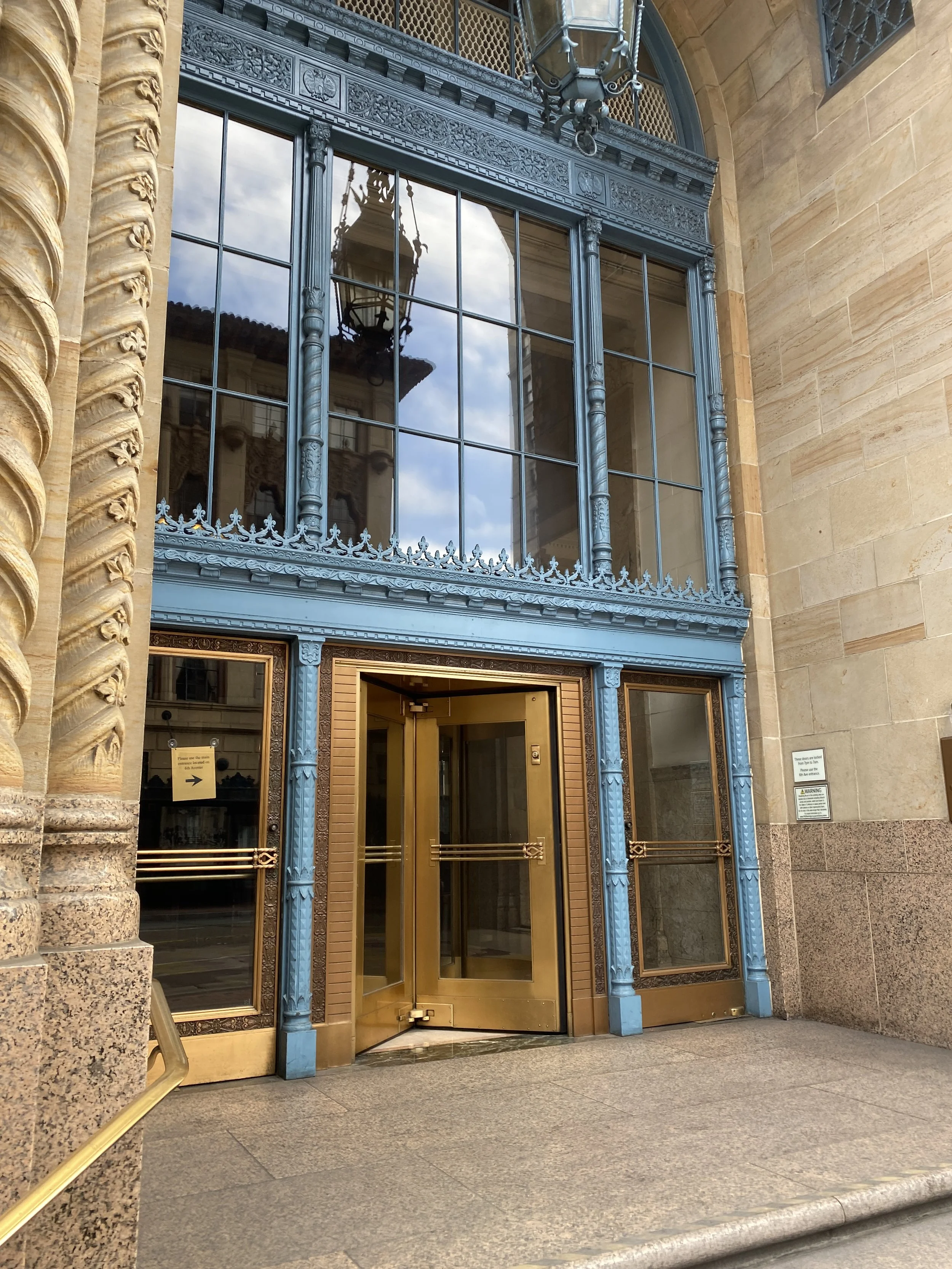Ornate historic entrance with blue metalwork, tall glass doors, and carved architectural details.