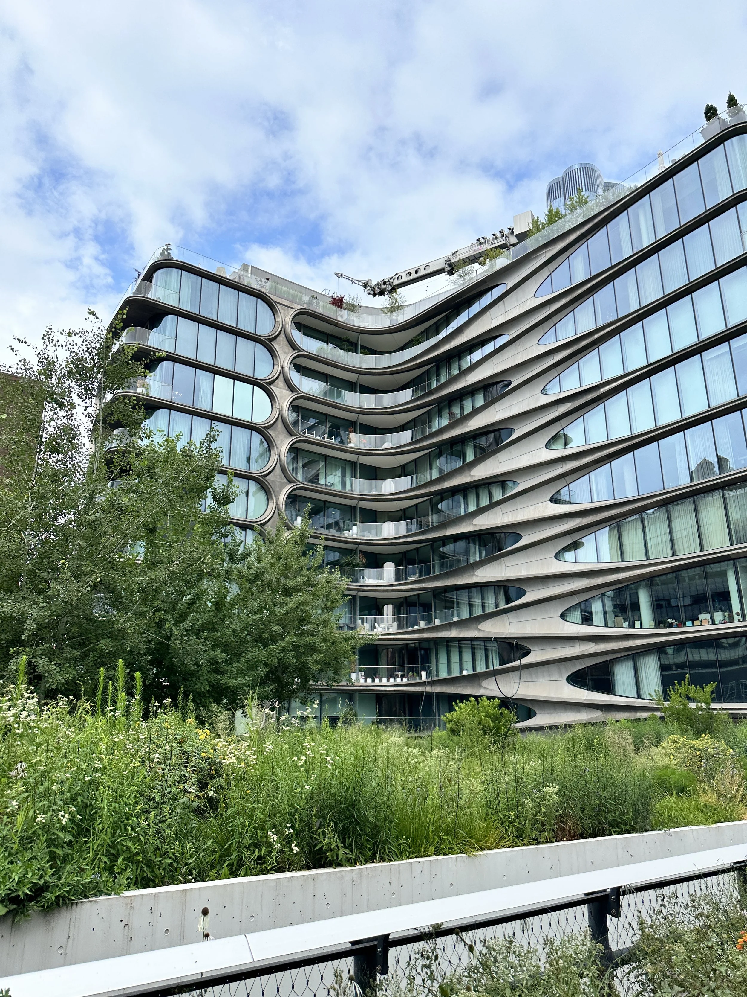 Curved contemporary building with layered balconies surrounded by lush landscaping.