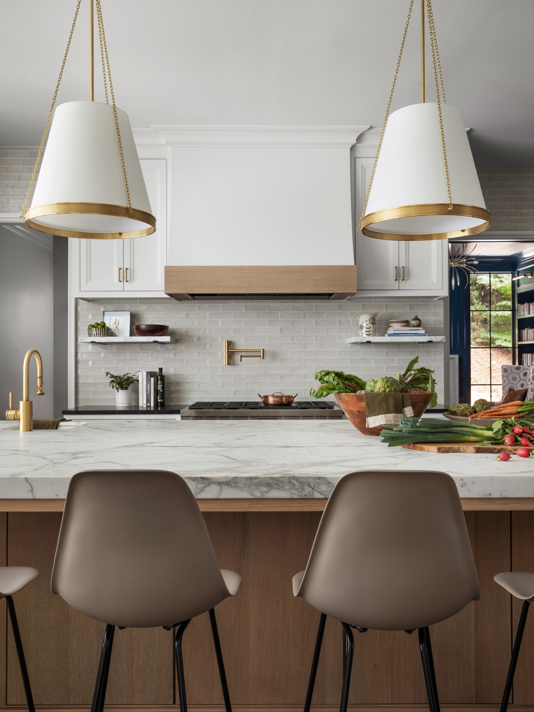 Custom kitchen with a marble waterfall island, natural wood cabinetry, white range hood, and brass pendant lighting.