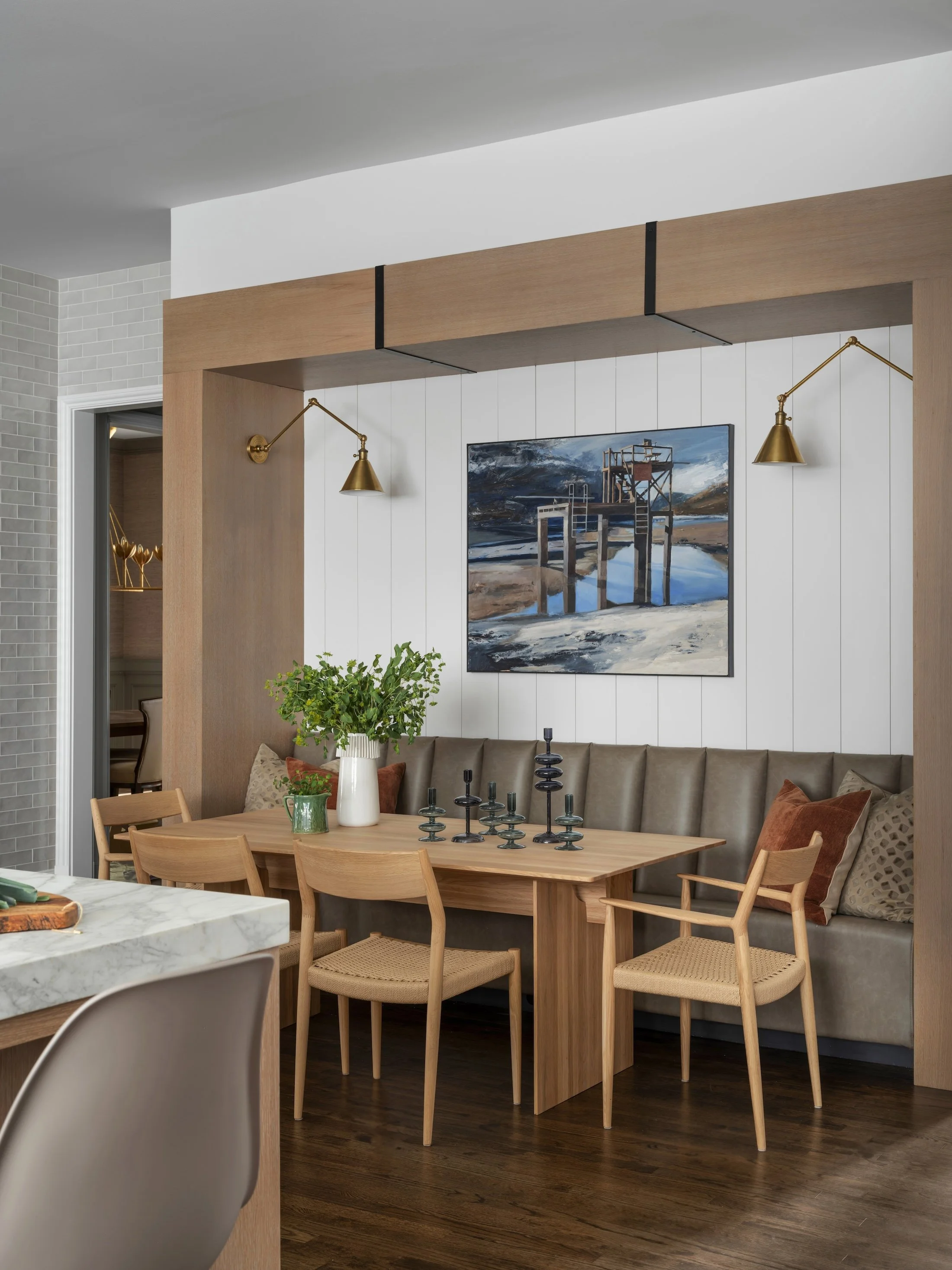 Built-in breakfast nook with a wood dining table, upholstered banquette, contemporary artwork, and brass sconces.