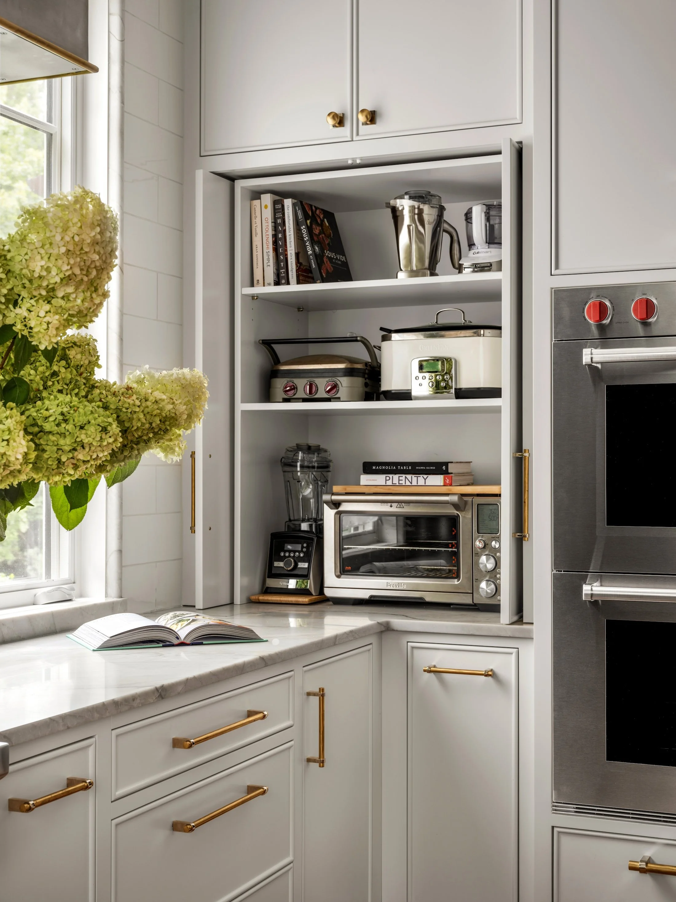Built-in kitchen appliance station with white cabinetry, open shelving, brass hardware, and small countertop appliances.