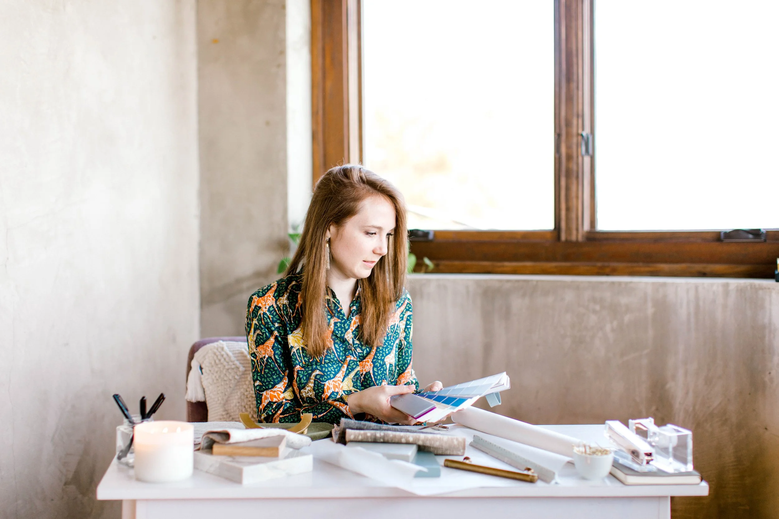 Crystal Dalton reviewing color swatches and material samples at a design table near a large window.