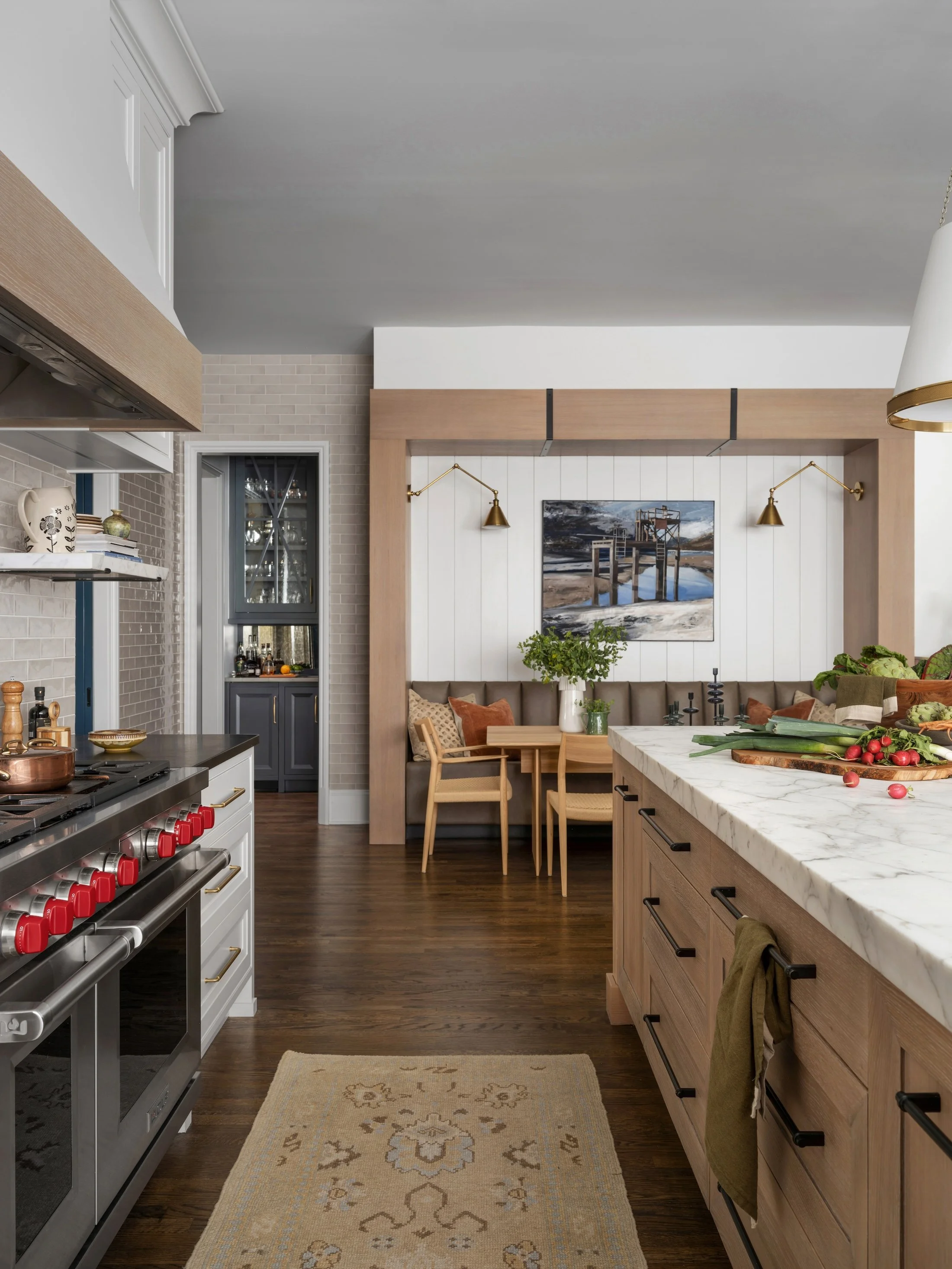View through a custom kitchen with a wood island, professional range, and an integrated breakfast nook beyond.