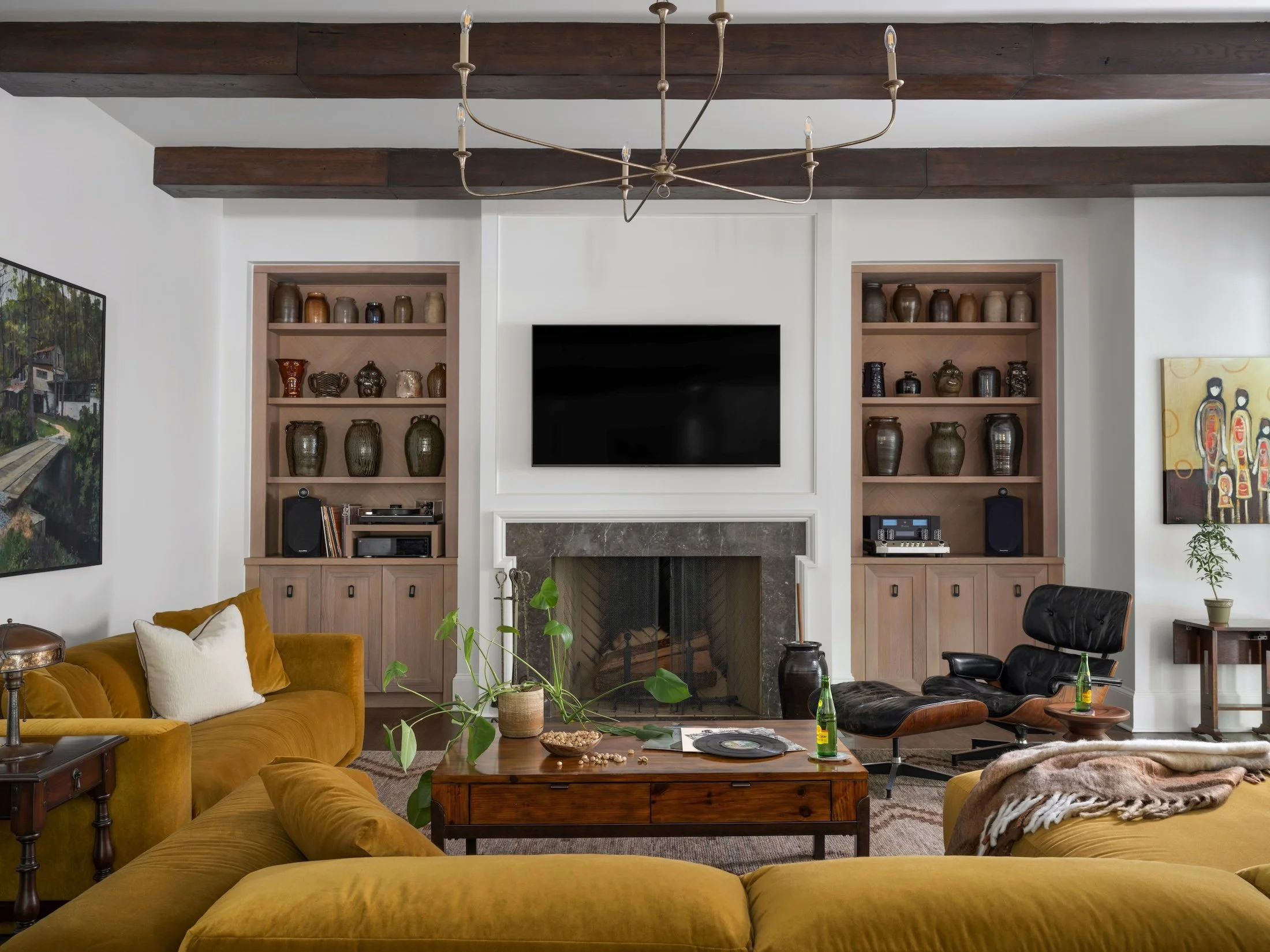Collected living room with a mustard velvet sofa, built-in wood shelving, fireplace, vintage-style coffee table, and black leather lounge chair.