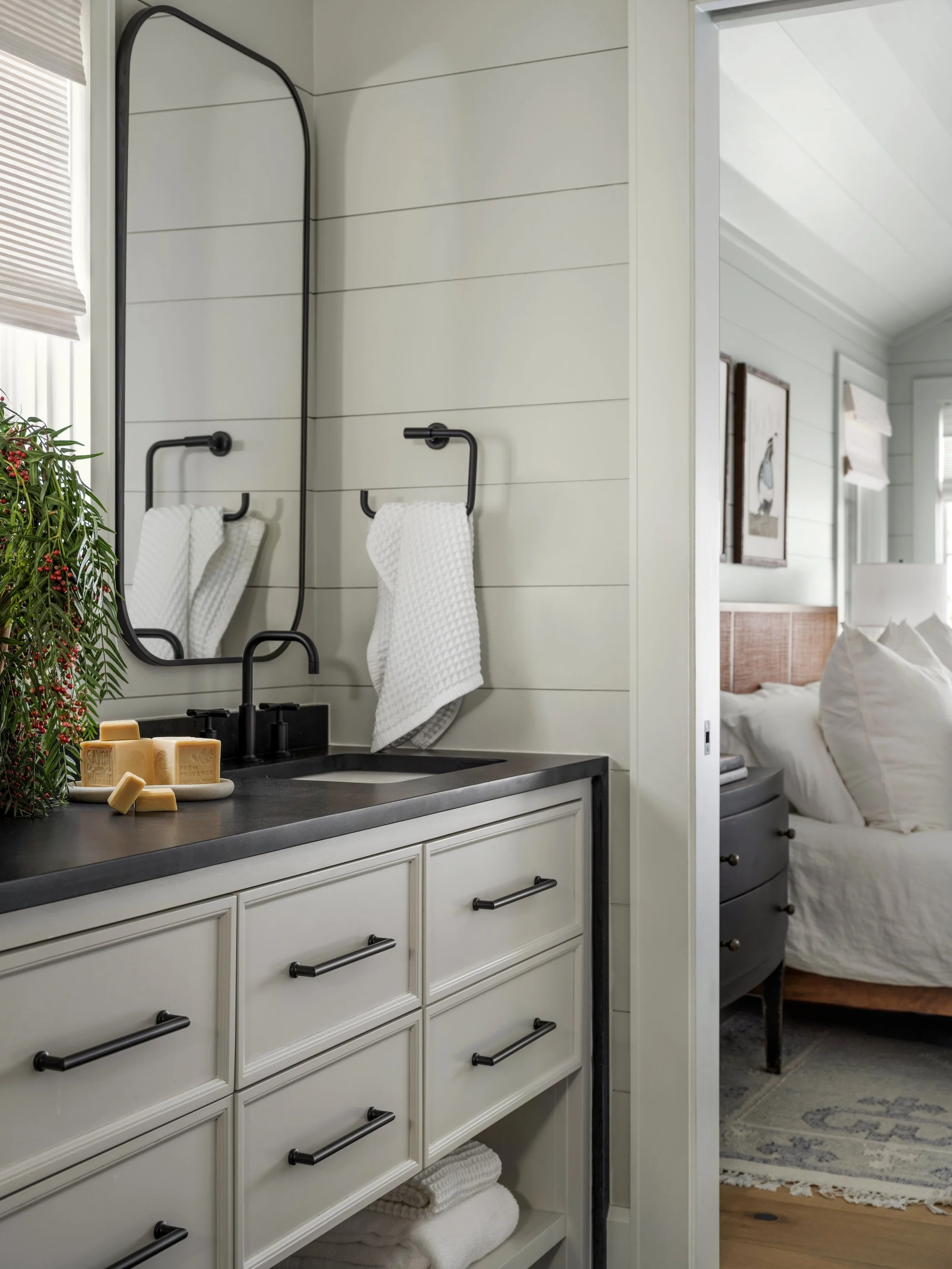 Compact bathroom vanity with white cabinetry, dark countertop, black fixtures, and shiplap walls.