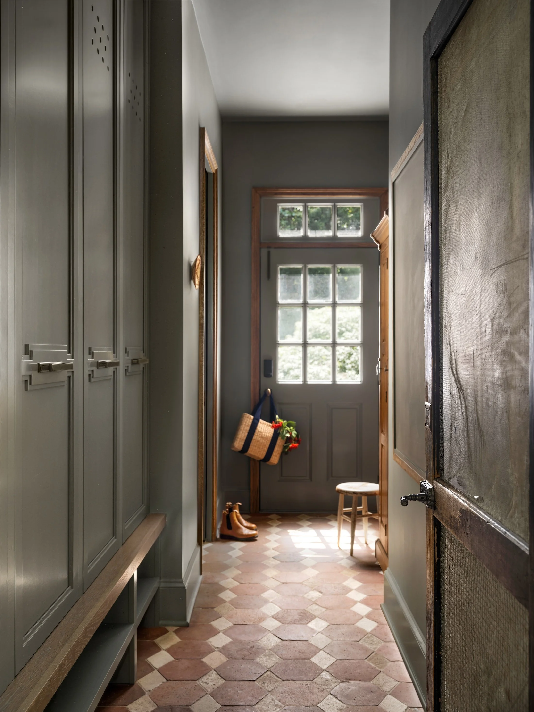 Dark painted mudroom hallway with built-in bench seating, patterned tile flooring, and a glass-paneled exterior door.