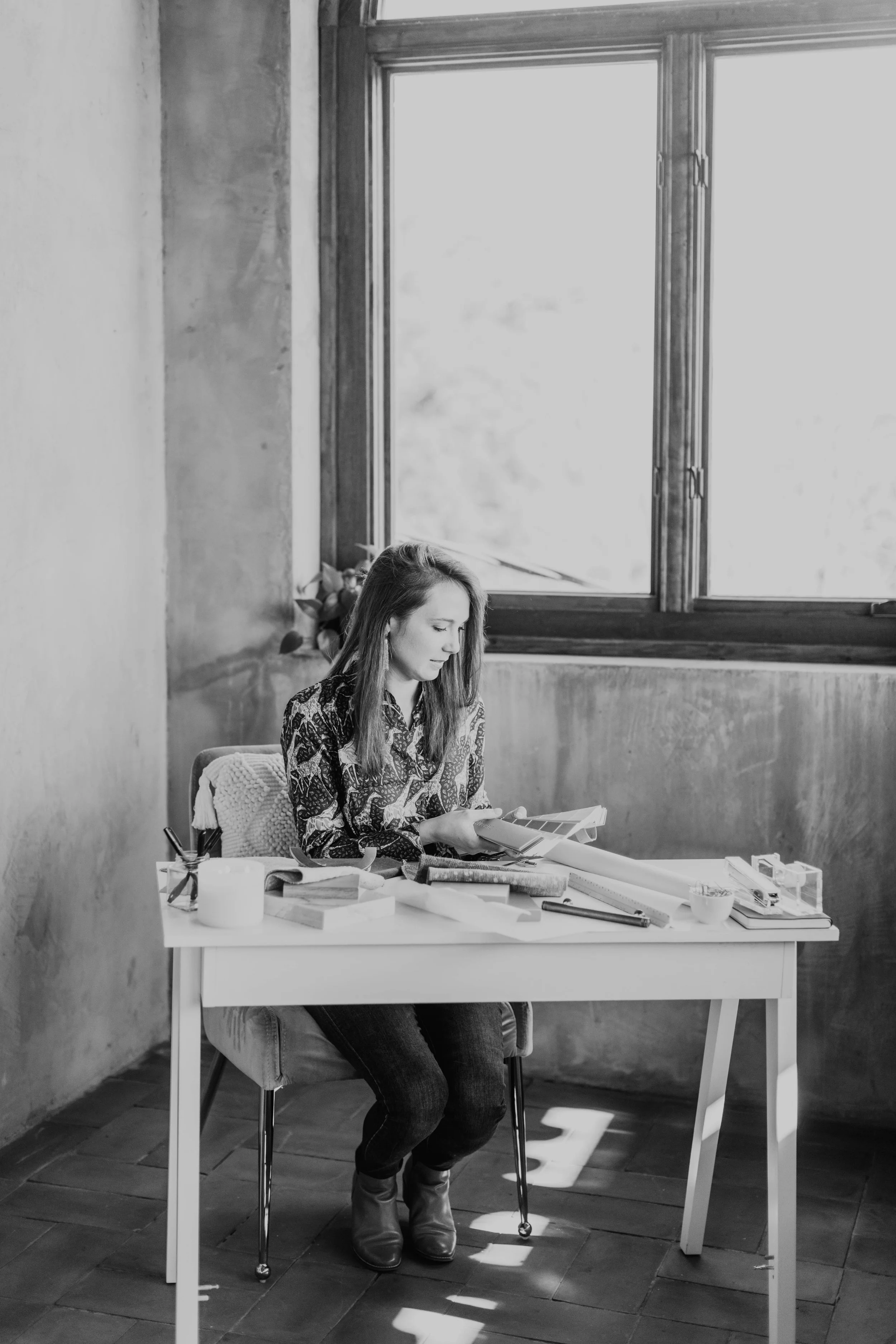 Black-and-white portrait of Crystal Dalton seated at a design table reviewing samples and project materials.