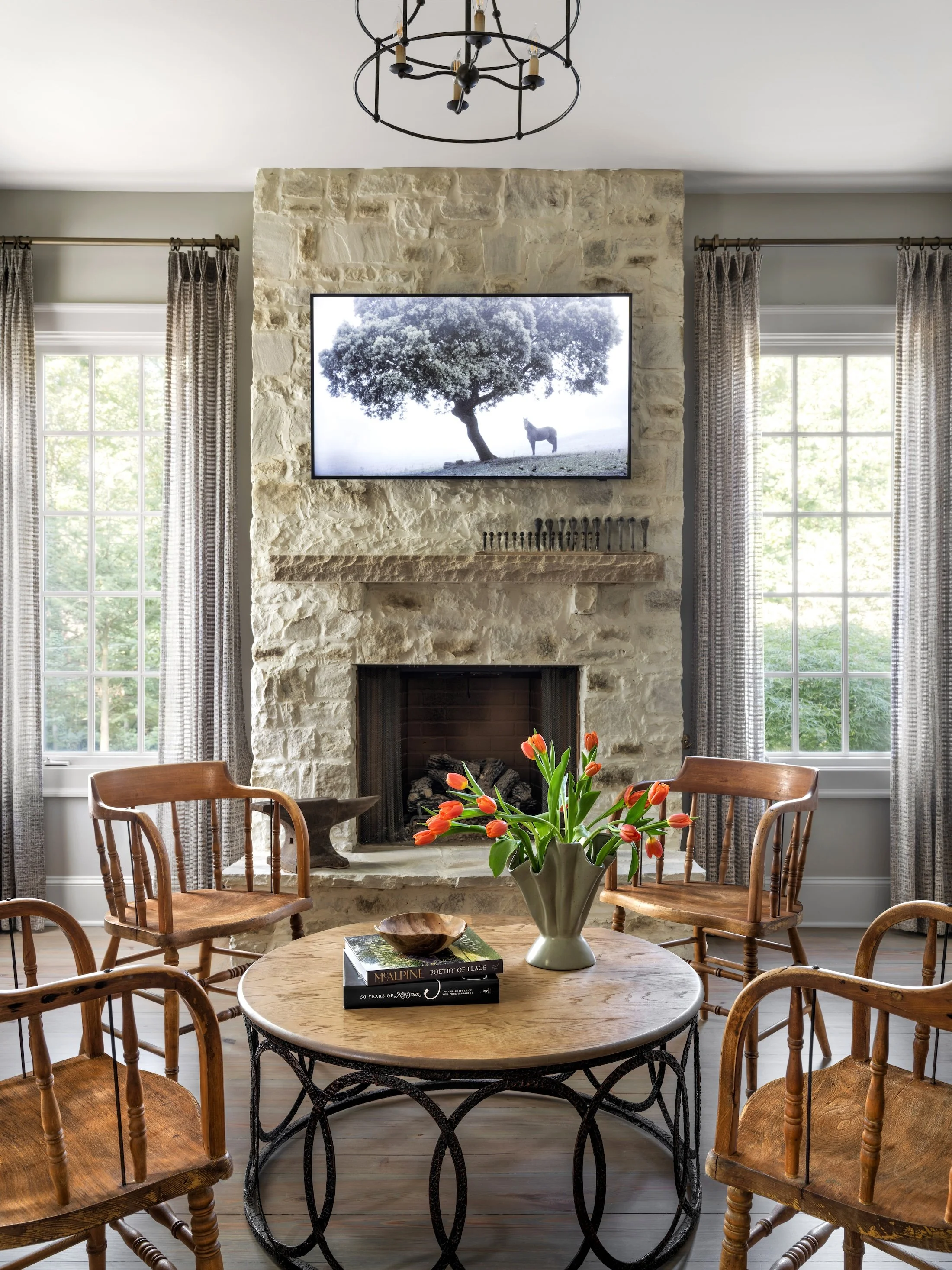 Cozy sitting room with a rustic stone fireplace, round table, wood chairs, and large windows.