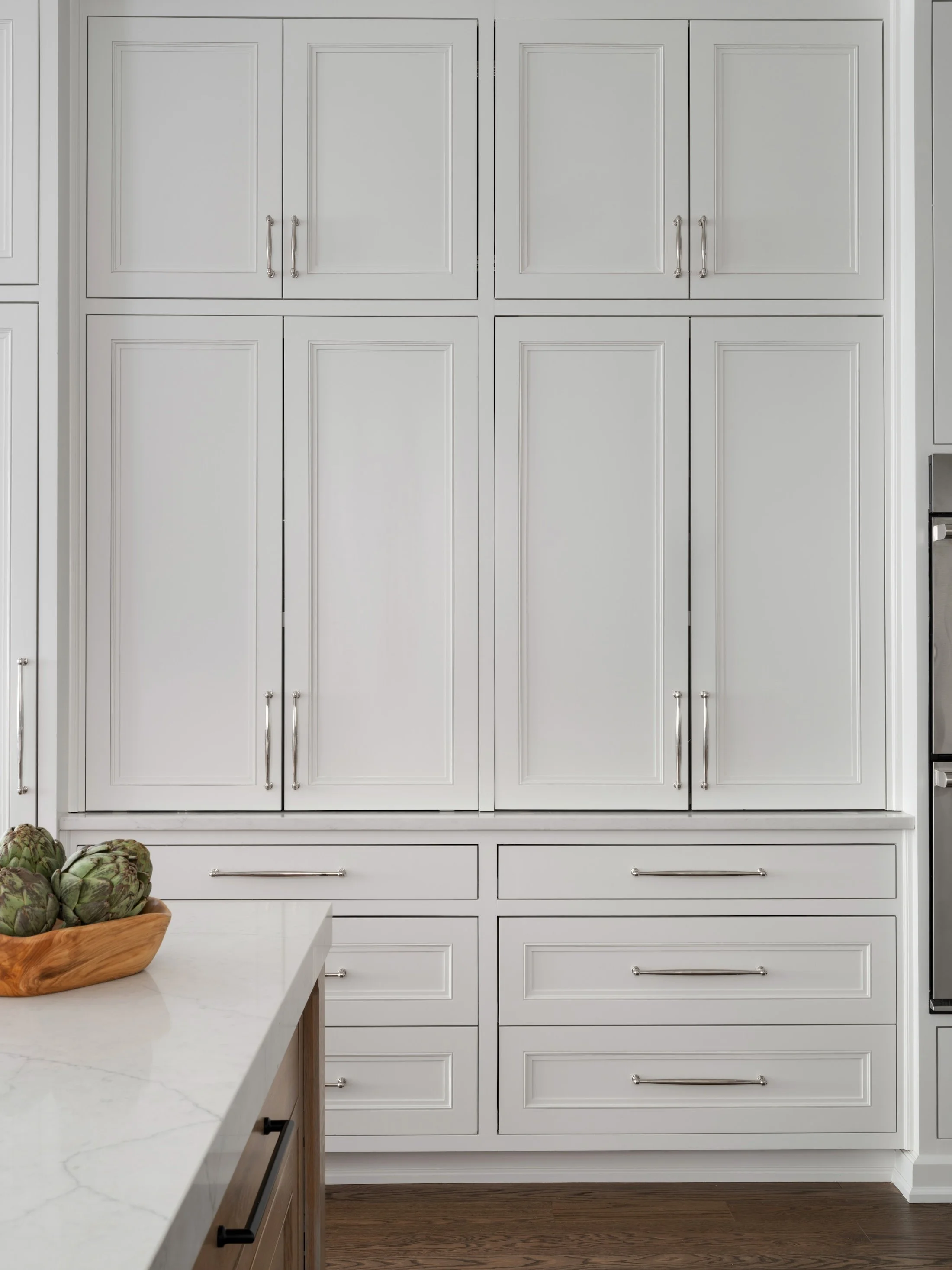 Floor-to-ceiling white kitchen cabinetry with integrated storage and slim metal hardware.