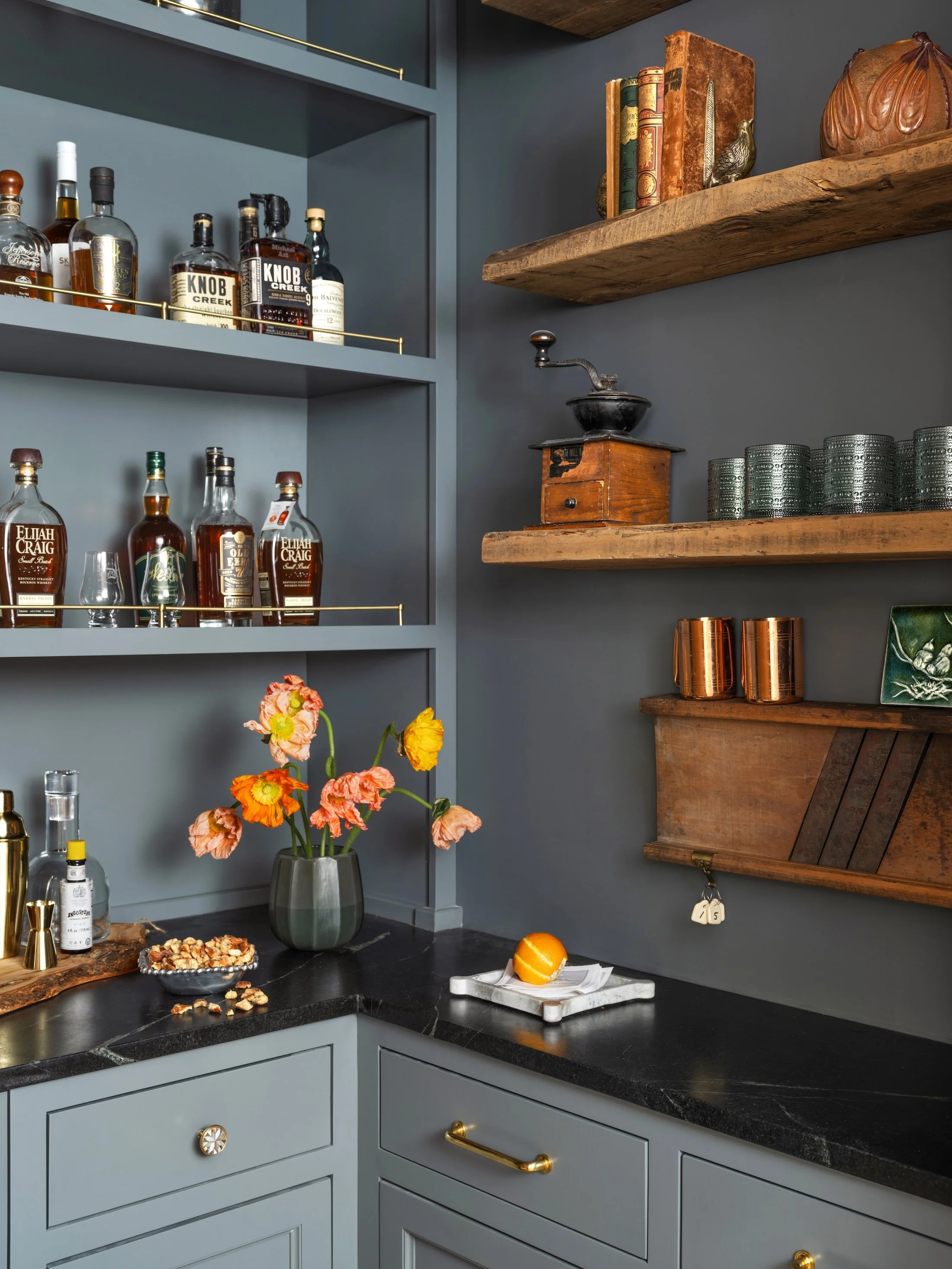 Moody blue home bar with open shelving, brass accents, dark countertops, and styled glassware.