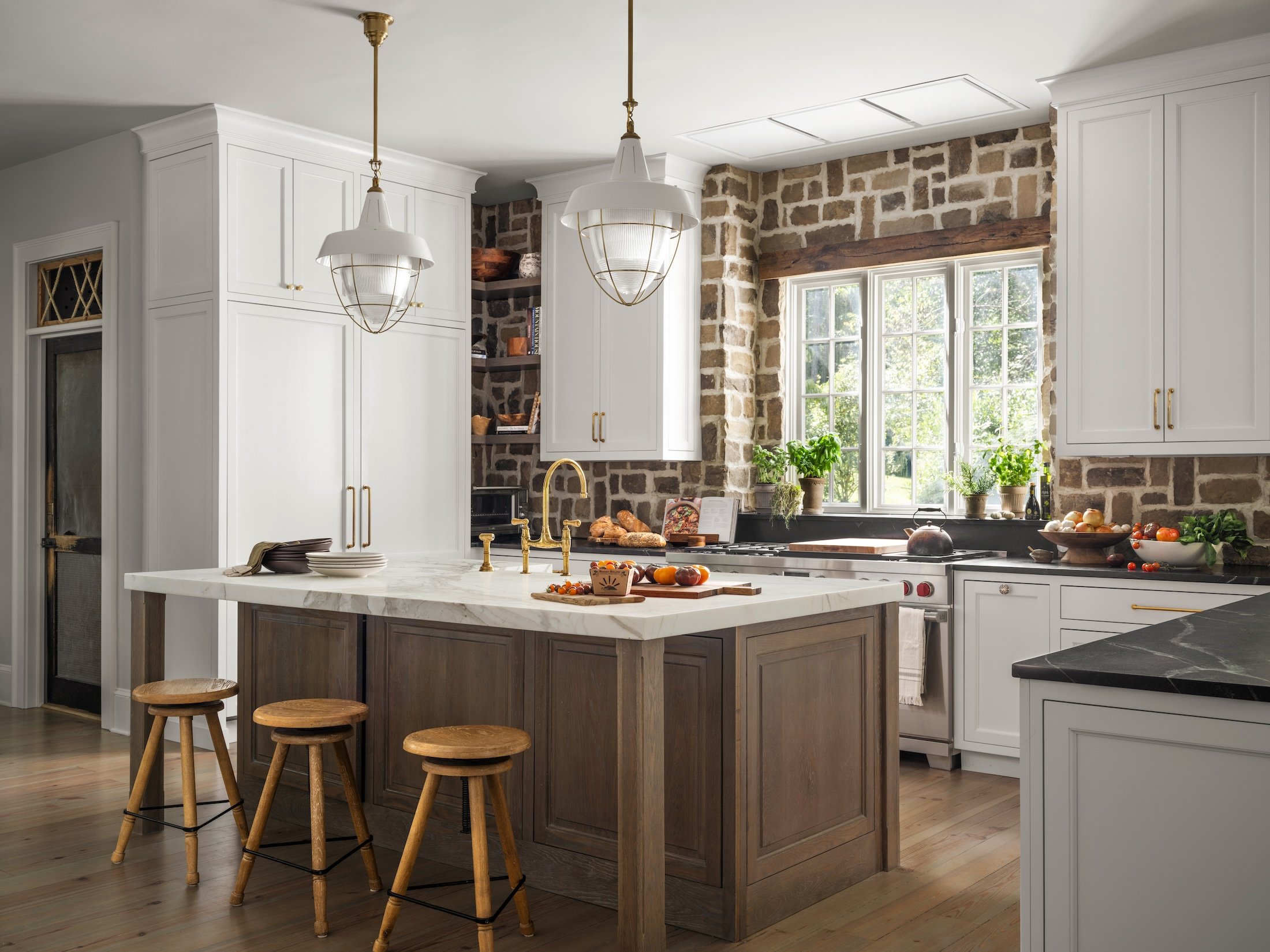 Bright kitchen with white cabinetry, natural wood island, stone accents, and large windows.