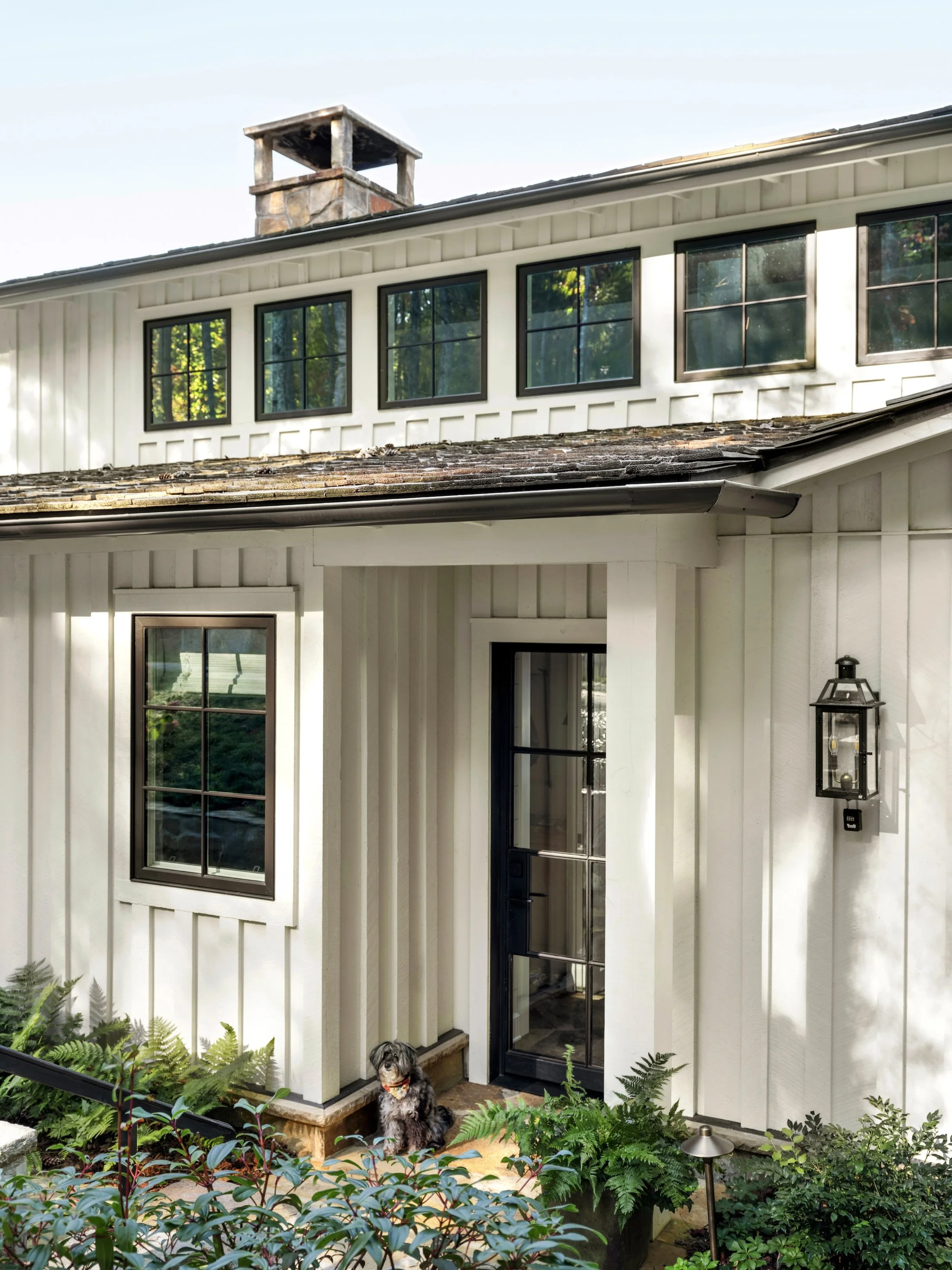 White cottage exterior with black-framed windows, layered rooflines, and rustic architectural details.