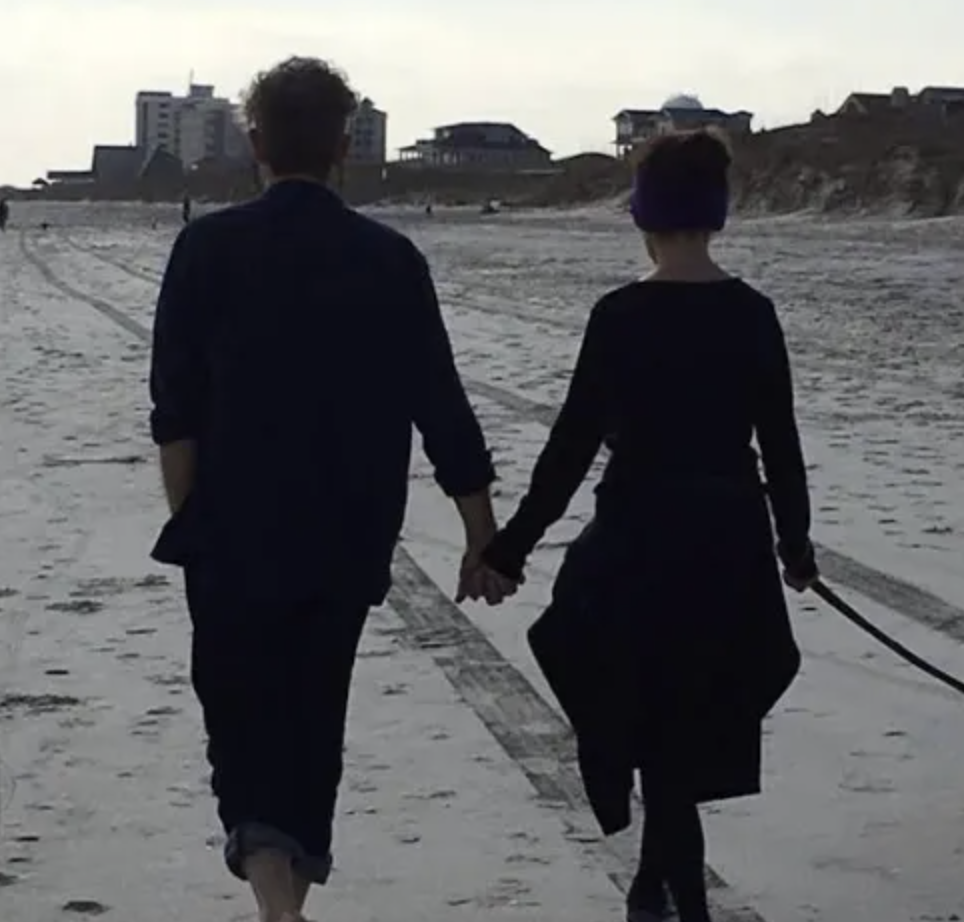 Two people holding hands while walking beside the water