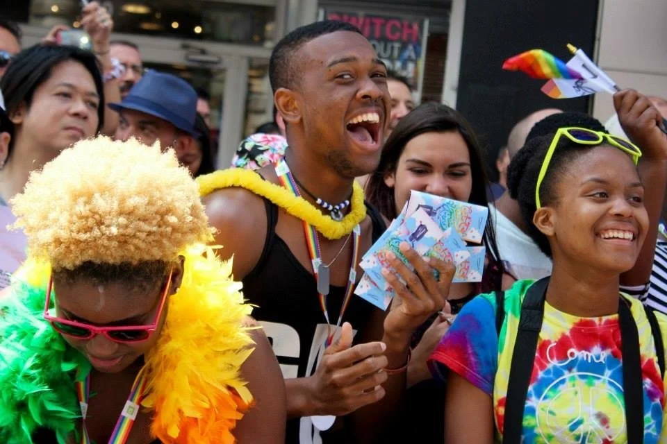 A diverse group of people celebrating at a Pride event, with rainbow flags, colorful clothing, and joyful expressions.