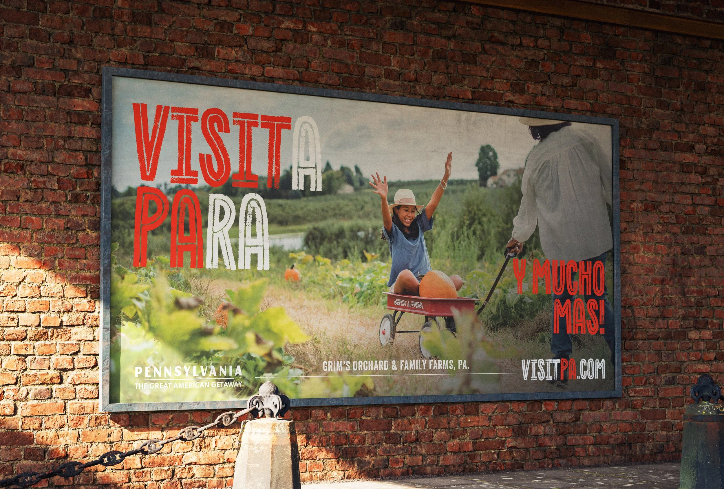 A billboard on a brick wall advertising a farm in Pennsylvania. It shows a woman and a girl with dark curly hair, the girl wearing a hat, riding a wagon through a green farm landscape with pumpkins. The woman is holding a device, possibly a camera or
