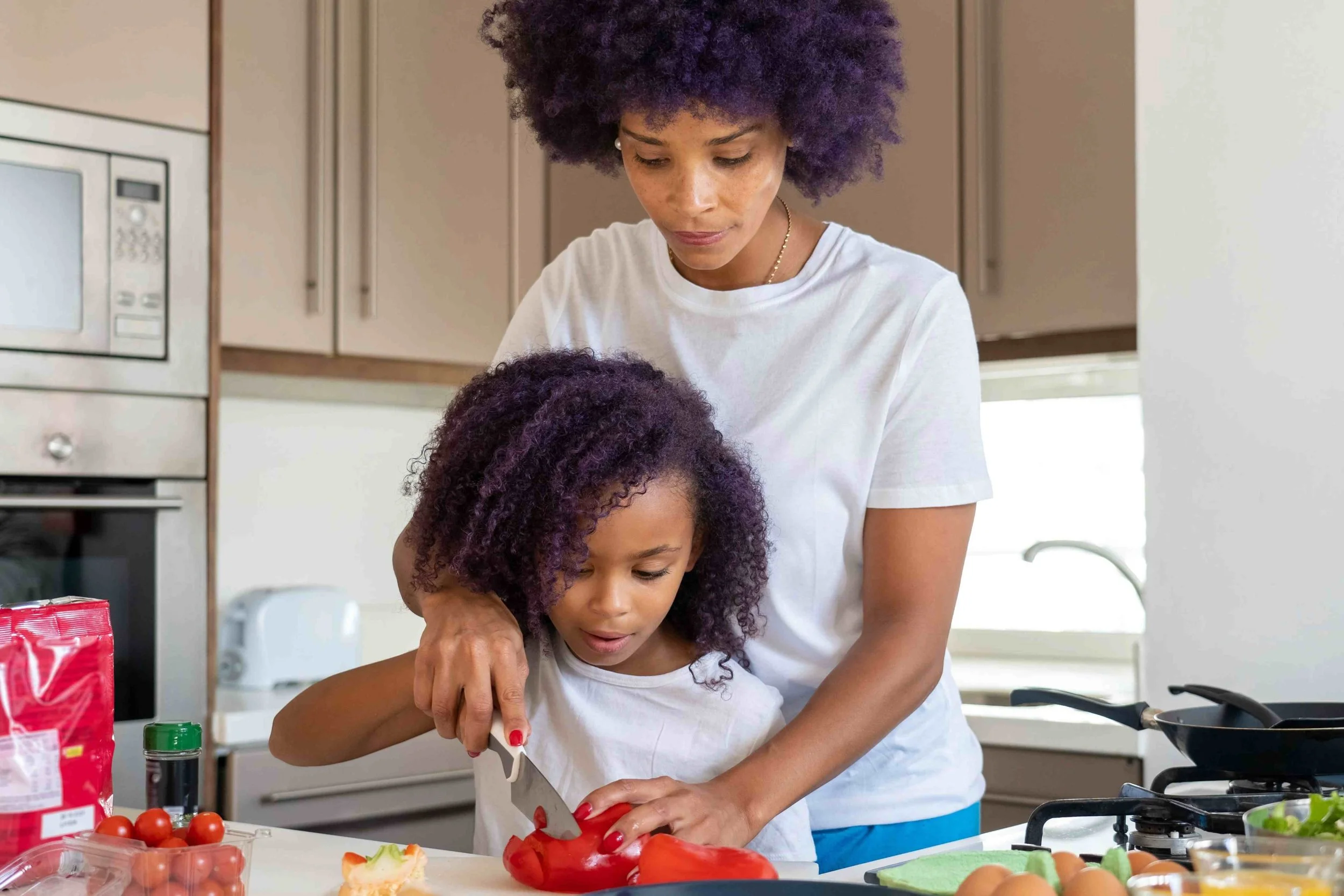 Mother teaching daughter ow to cut tomatoes