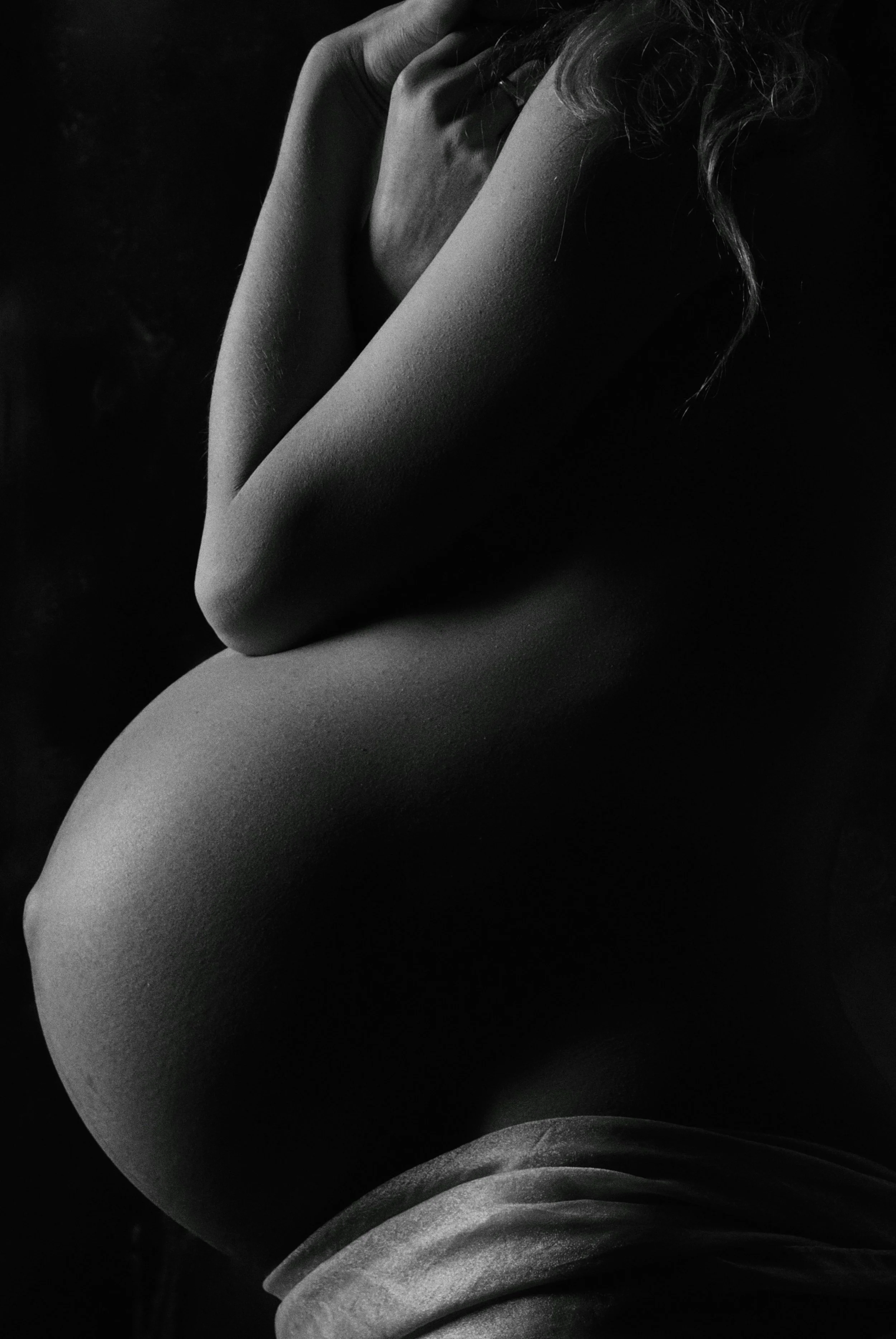 A black and white photograph of a person with their arms crossed, covering part of their face, with visible curly hair and textured skin.